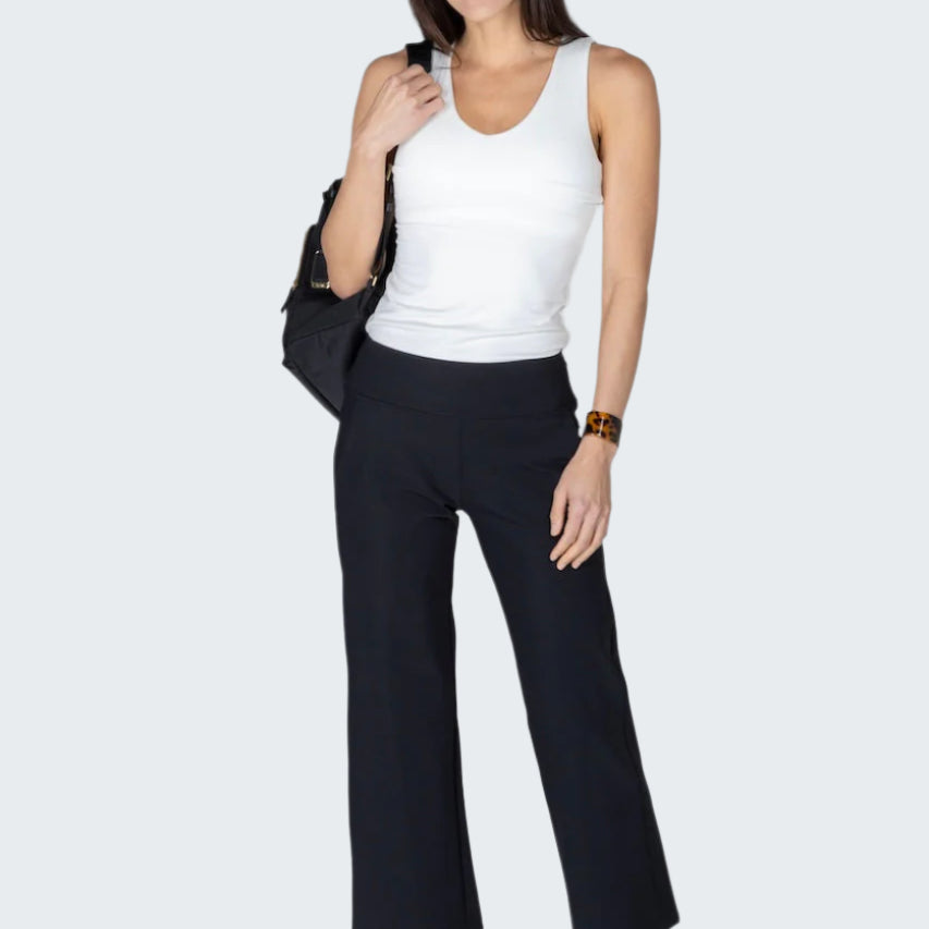 Woman wearing a white tank top and black pants on a plain background