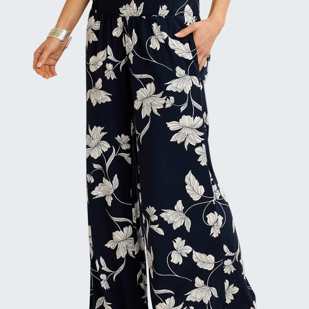 Navy blue pants with white floral pattern worn by a person on a beige background