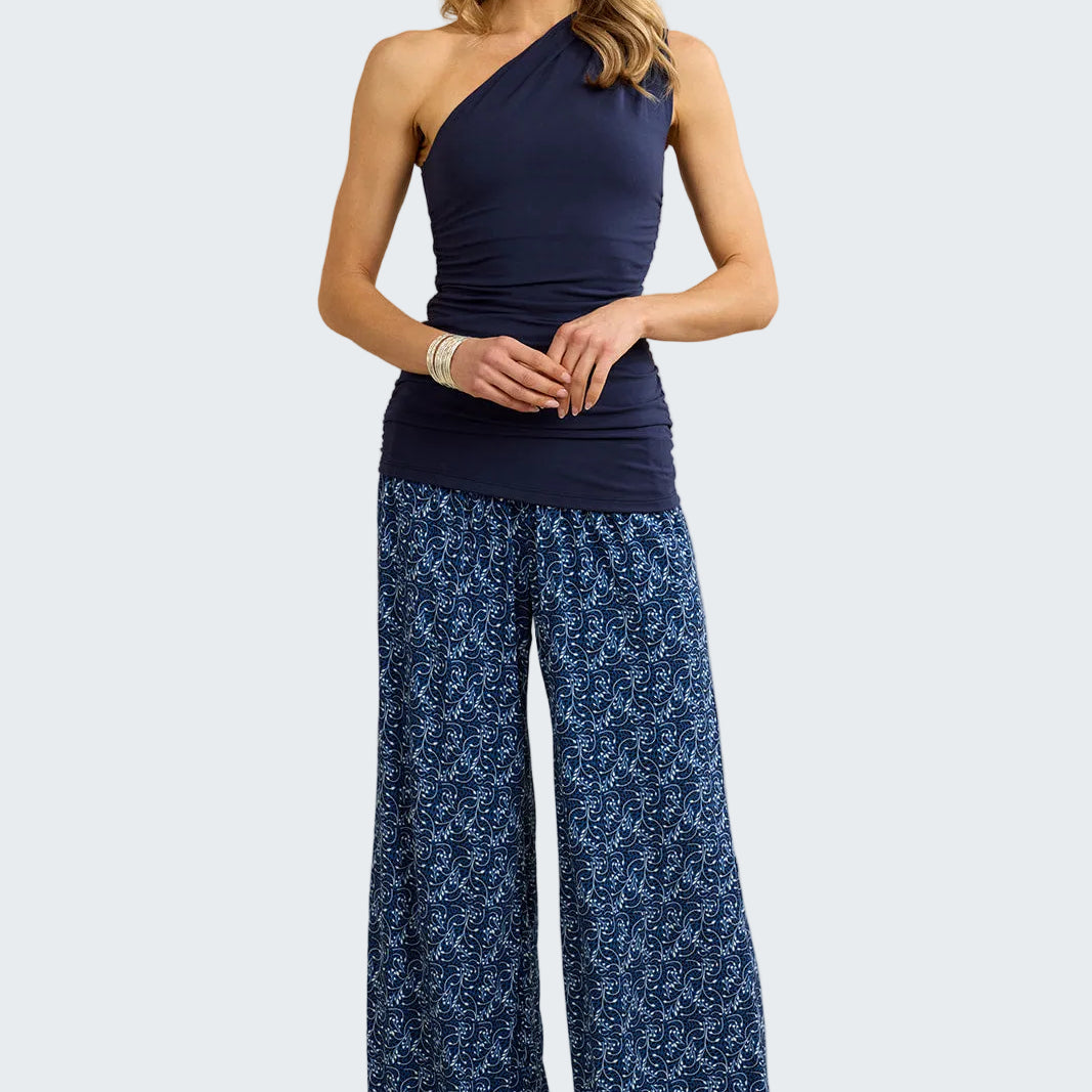 Woman wearing a navy one-shoulder top and blue patterned pants against a beige background