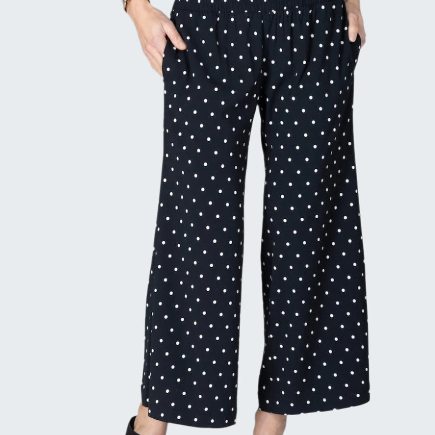 Black pants with white polka dot pattern worn by a person on a light gray background