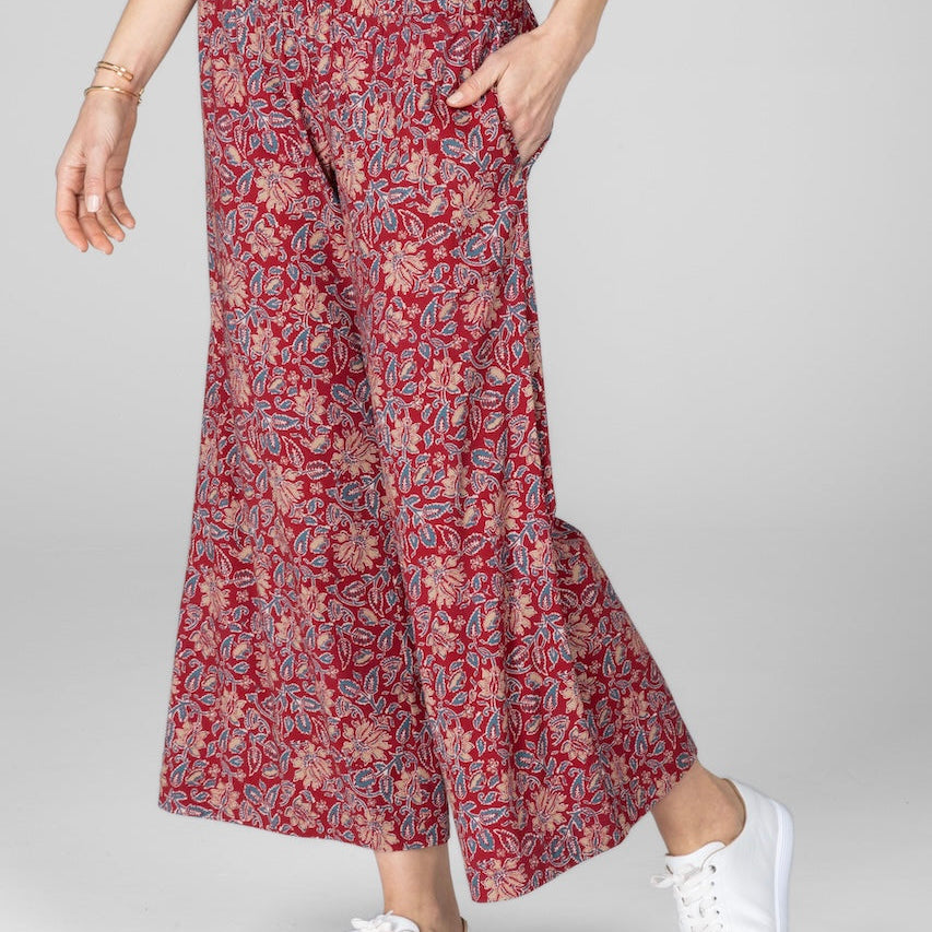Person wearing red floral wide-leg pants with a white top and white sneakers on a light gray background