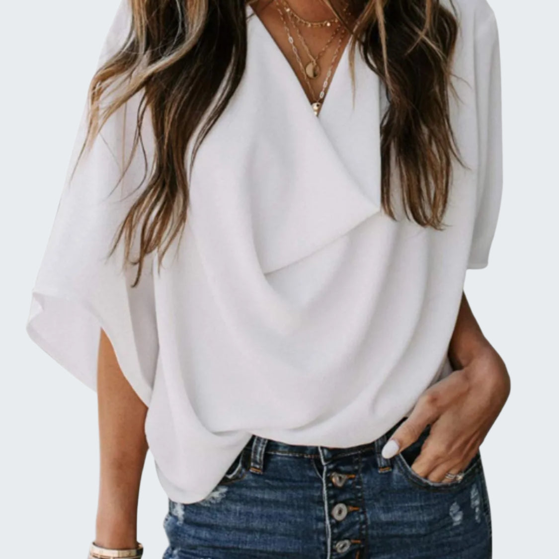 A woman wearing a white ruched three-quarter sleeve blouse with a V-neckline, paired with blue jeans.