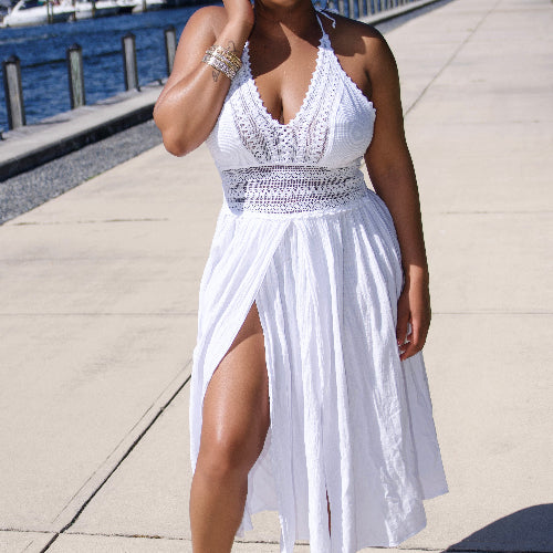 Woman in a white dress standing on a sidewalk by a waterfront.