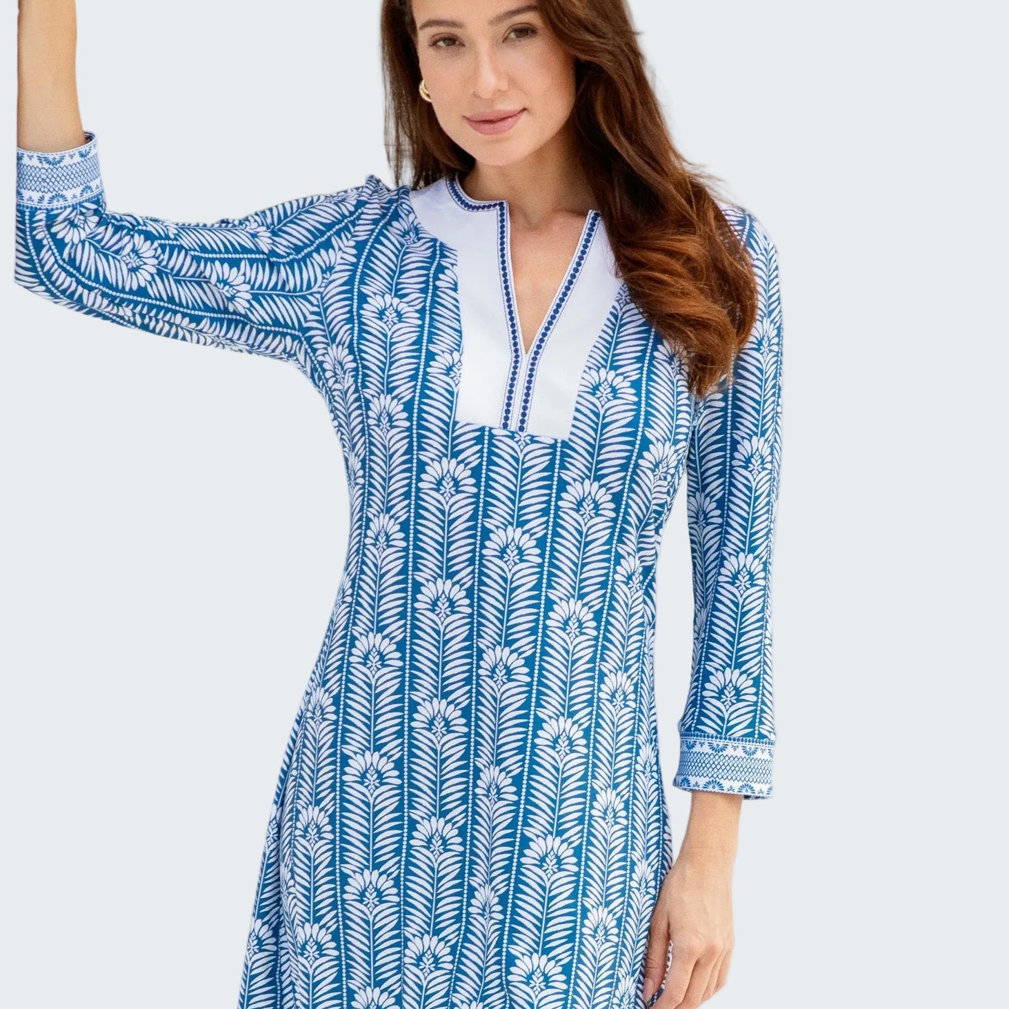 Woman wearing a blue and white patterned dress standing in front of a white wall.