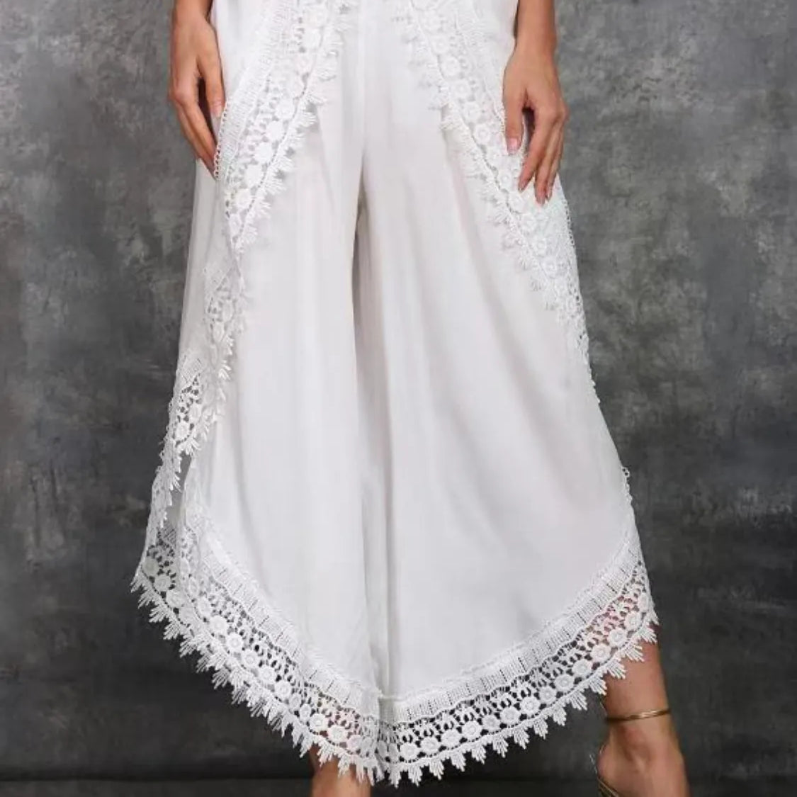 White wide leg pants with lace detailing at the hem, shown on a model wearing high heels.