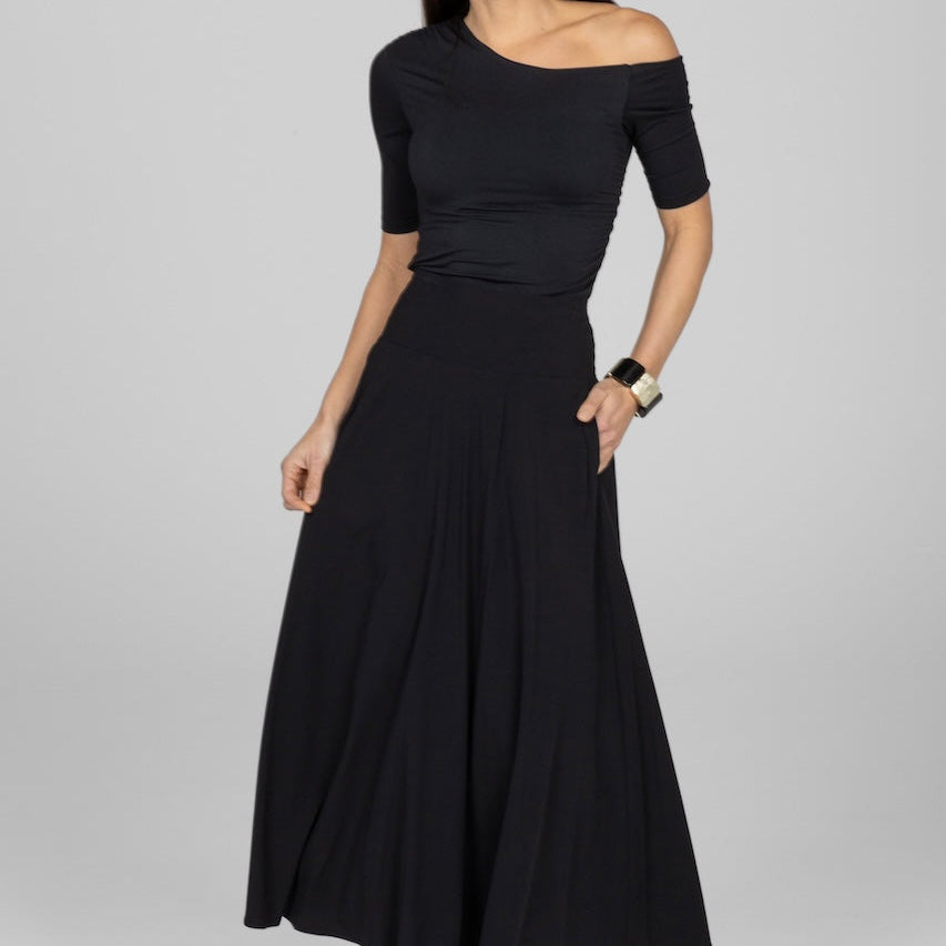 Woman wearing a black off-shoulder top and long skirt on a gray background