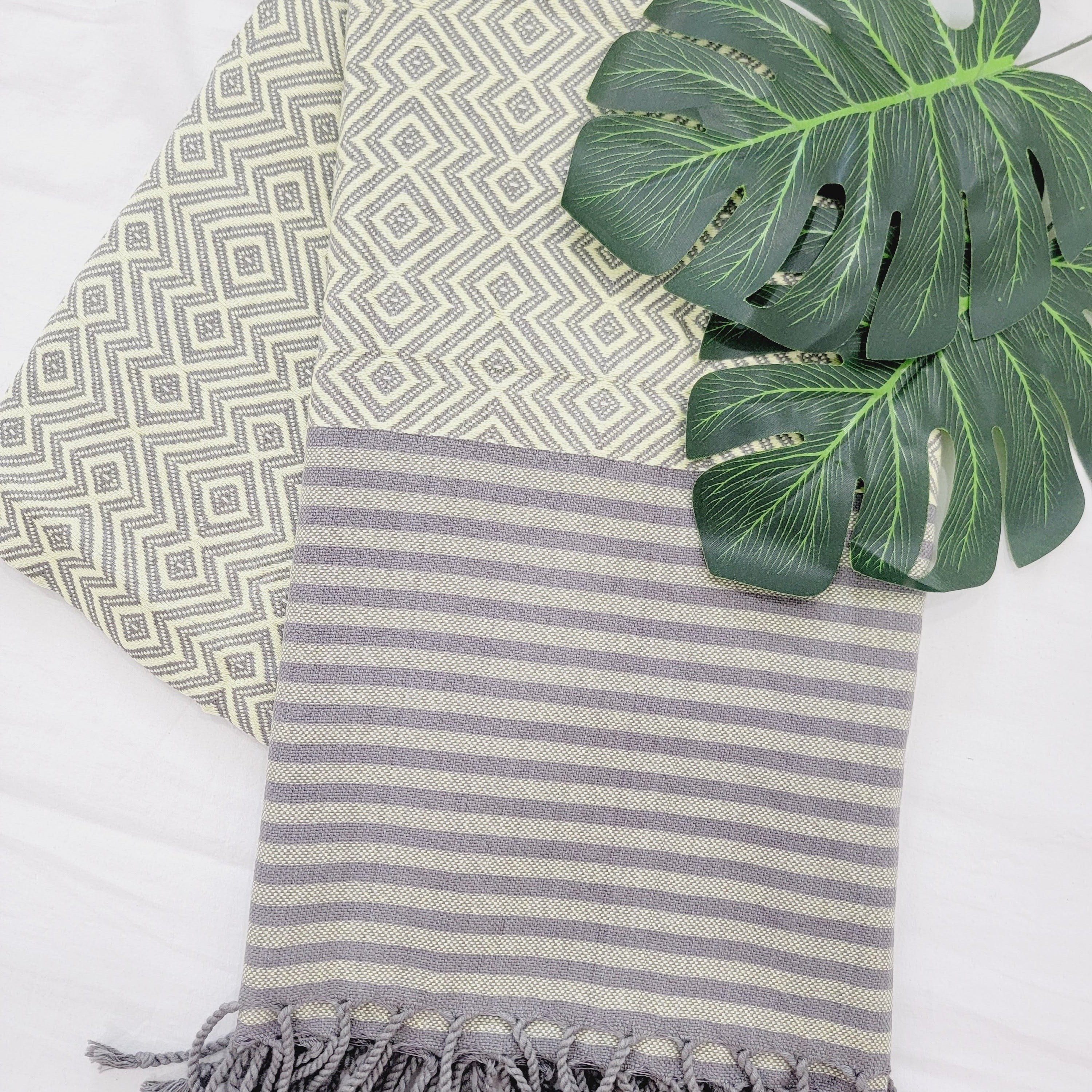 Two patterned towels with tassels and a green leaf on a white background