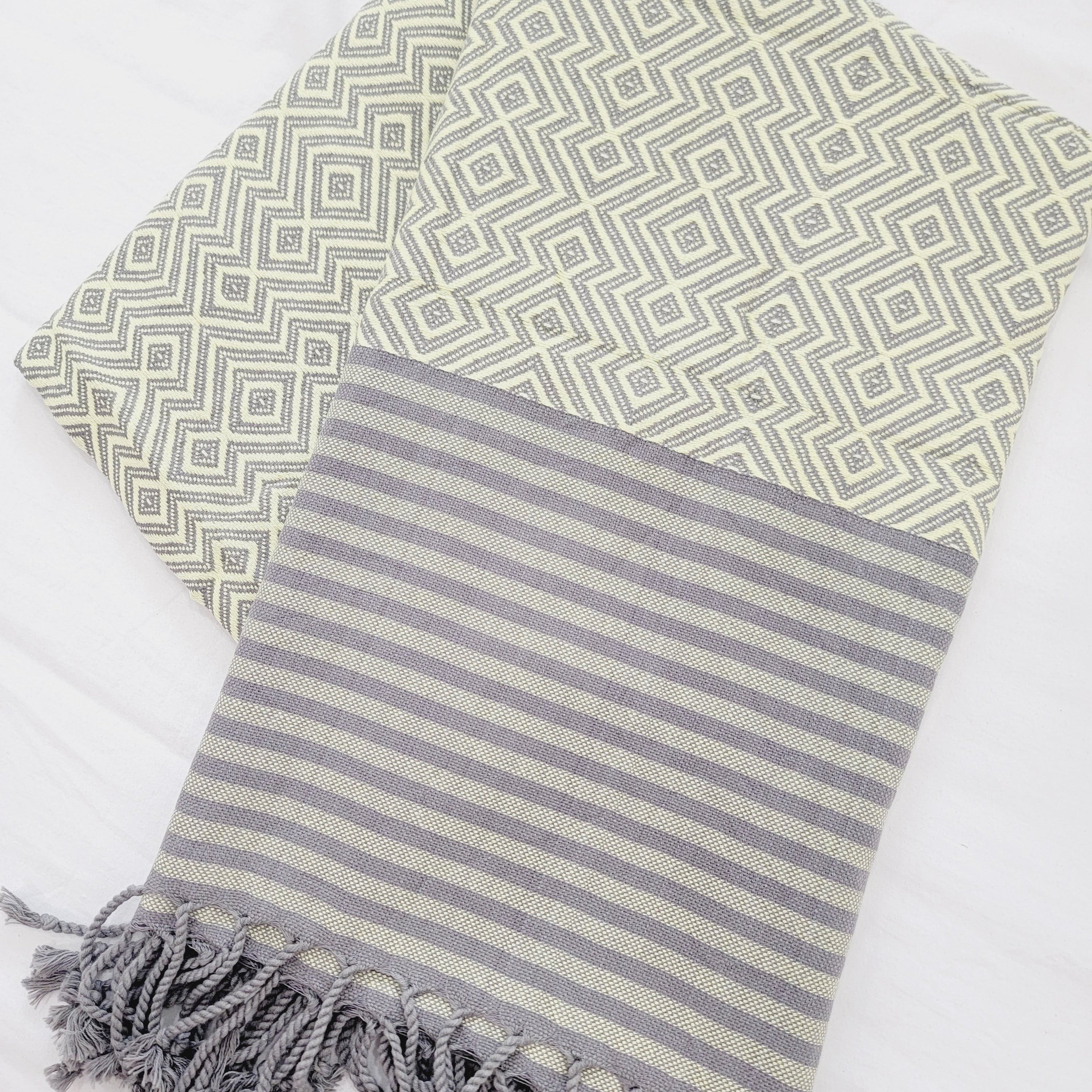 Two patterned towels, one green with geometric design and the other gray with stripes, on a white background.