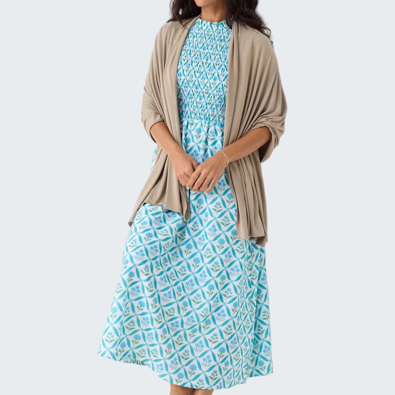 Woman wearing a blue patterned dress with a beige cardigan against a white background