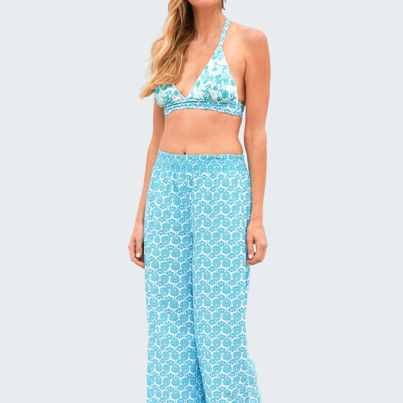 Woman wearing a blue patterned bikini and pants on a beach