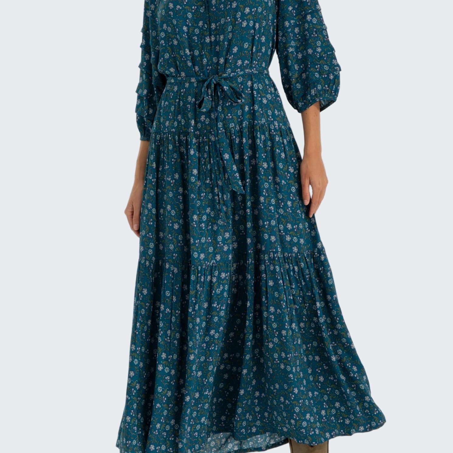 Woman wearing a long teal dress with a pattern on a white background