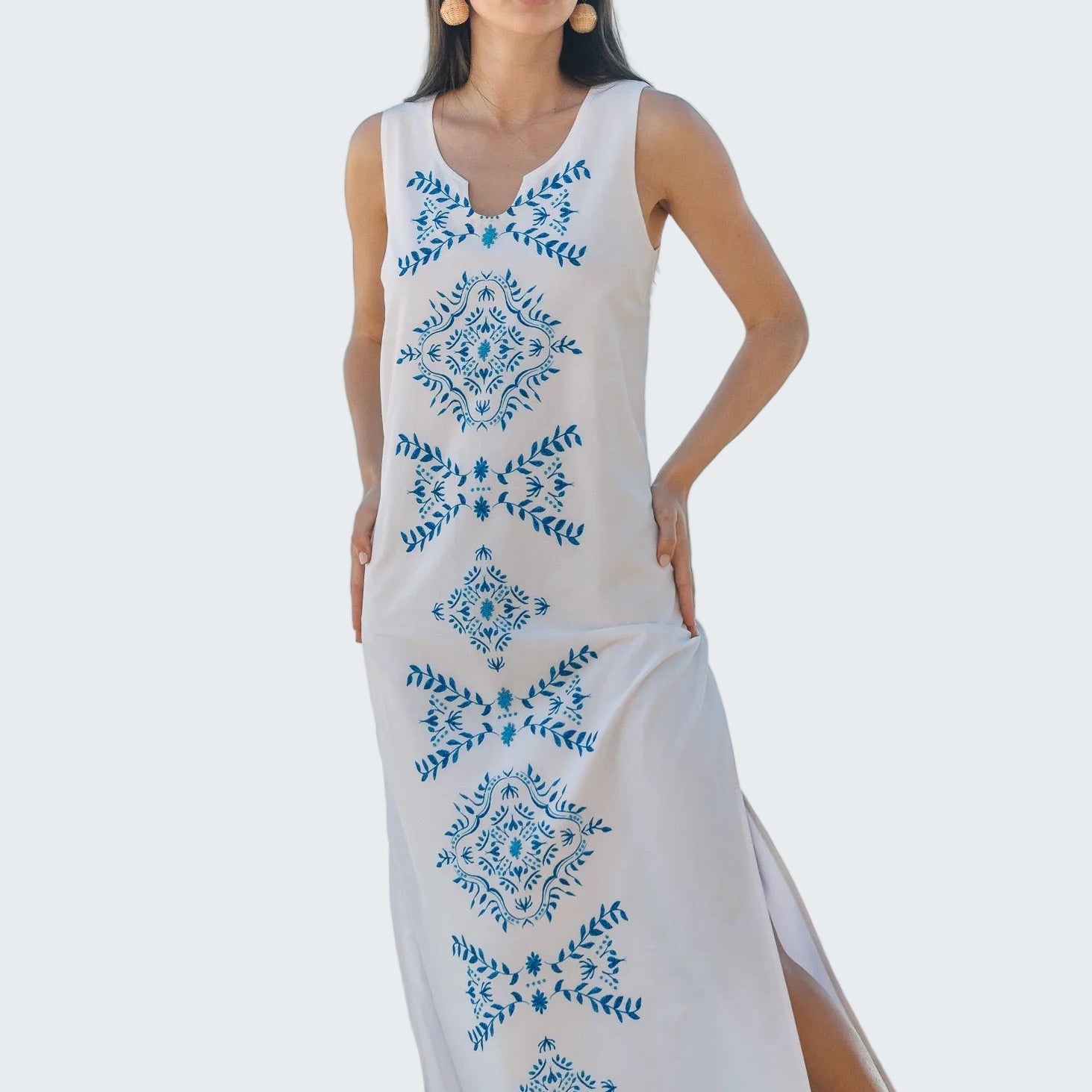 Woman wearing a white dress with blue floral patterns on a beach.