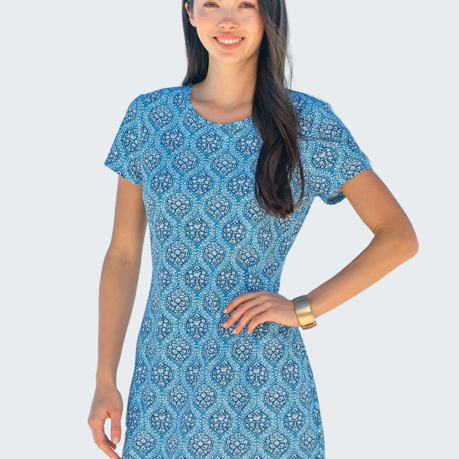 Woman wearing a blue patterned dress standing on a beach with ocean in the background