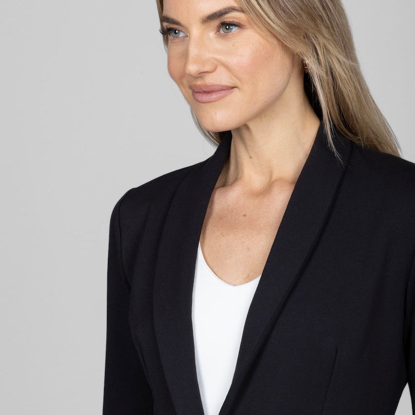 Woman wearing a black blazer over a white top against a plain background