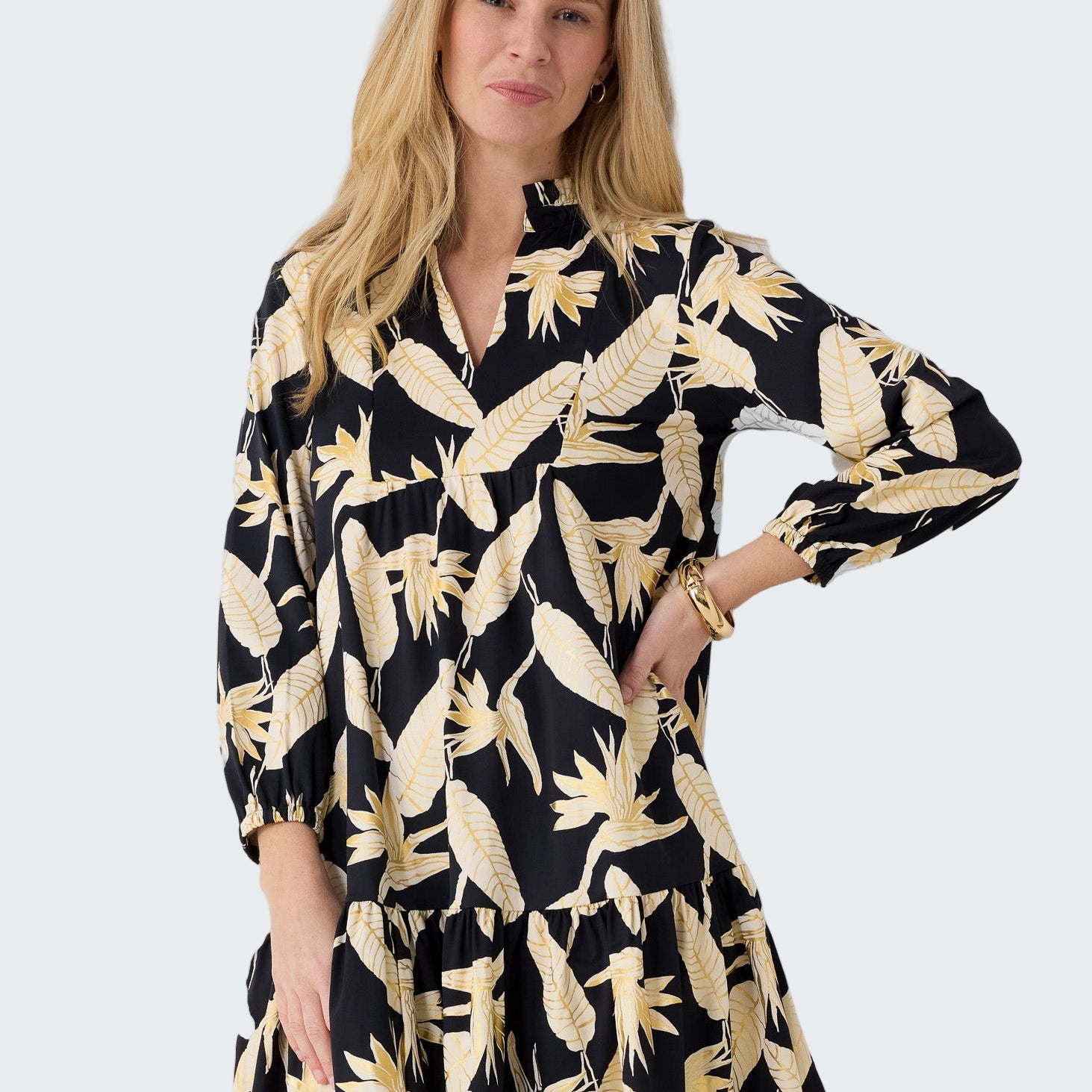 Woman wearing a black dress with gold floral pattern against a white background