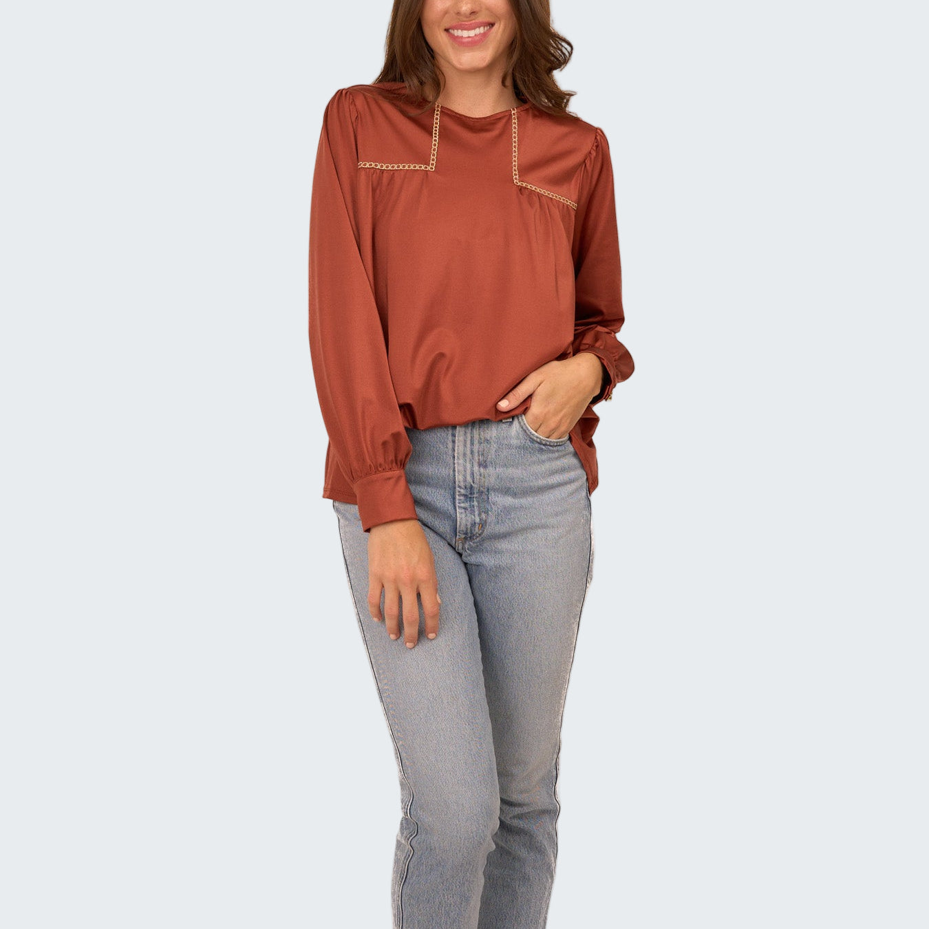 Woman wearing a rust-colored blouse and light blue jeans on a white background