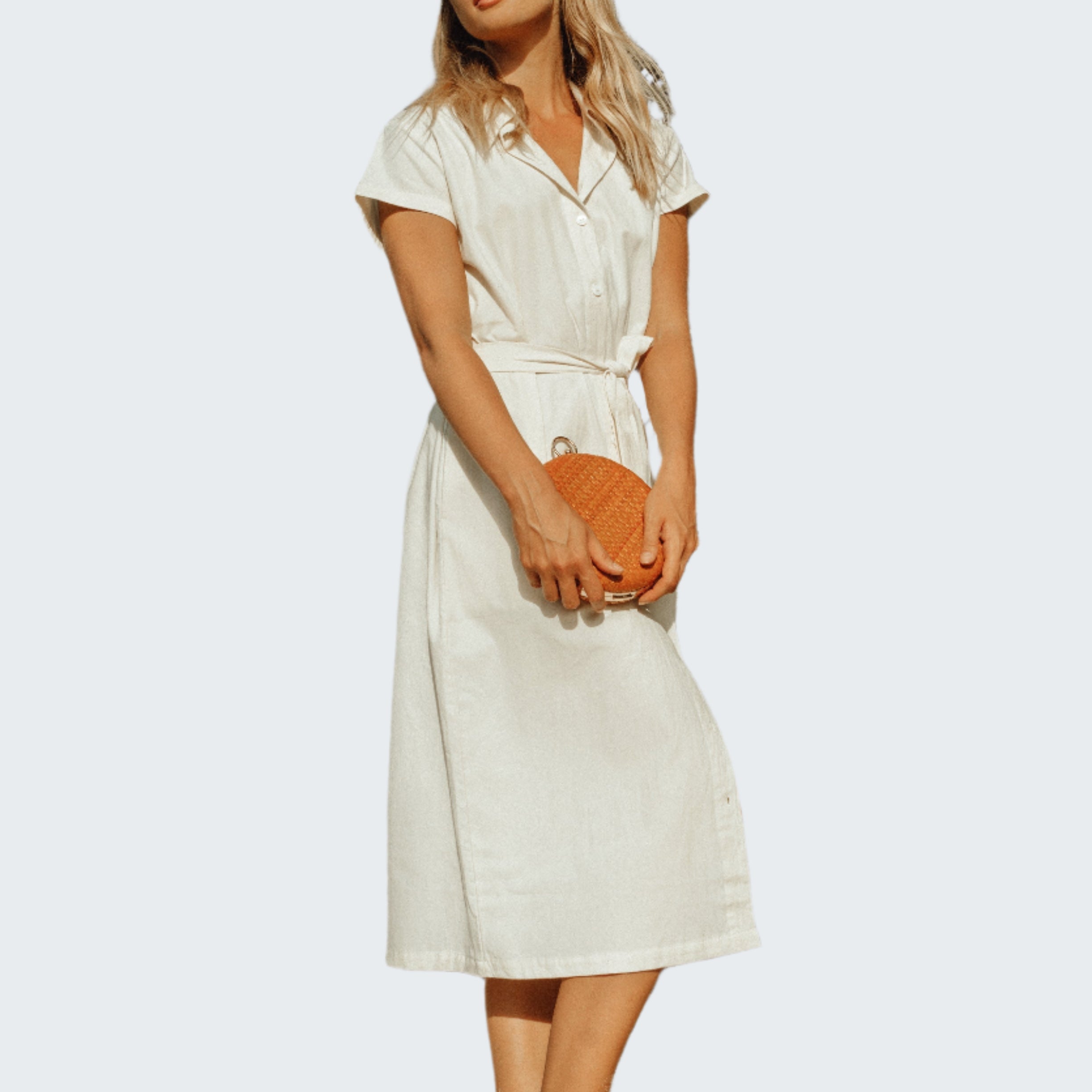 Woman in a white dress standing against a rocky wall.