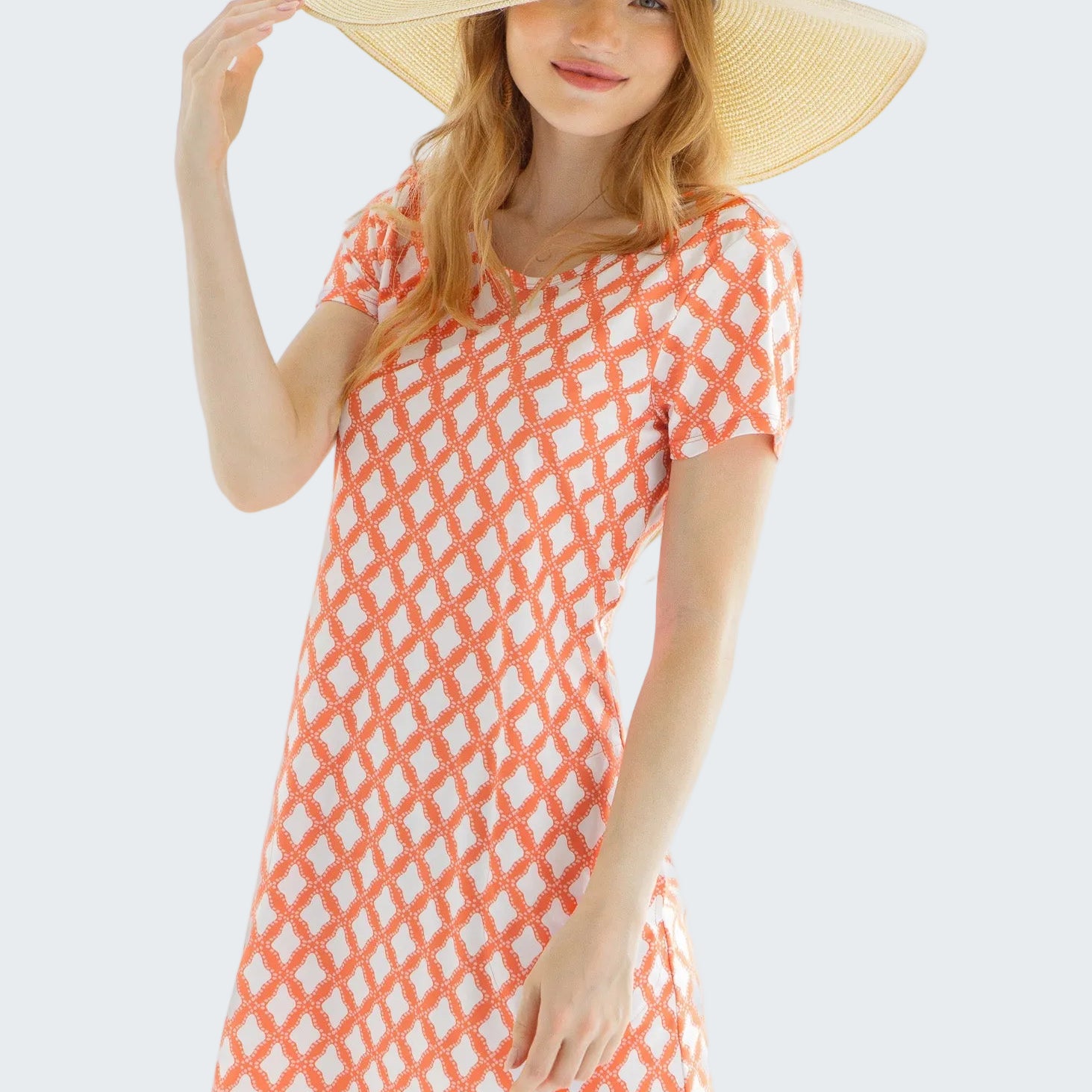 Woman wearing a coral patterned dress and wide-brimmed hat against a white background