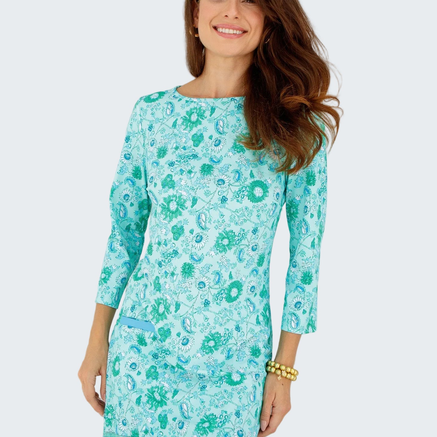 Woman wearing a turquoise floral dress standing in front of a white window.