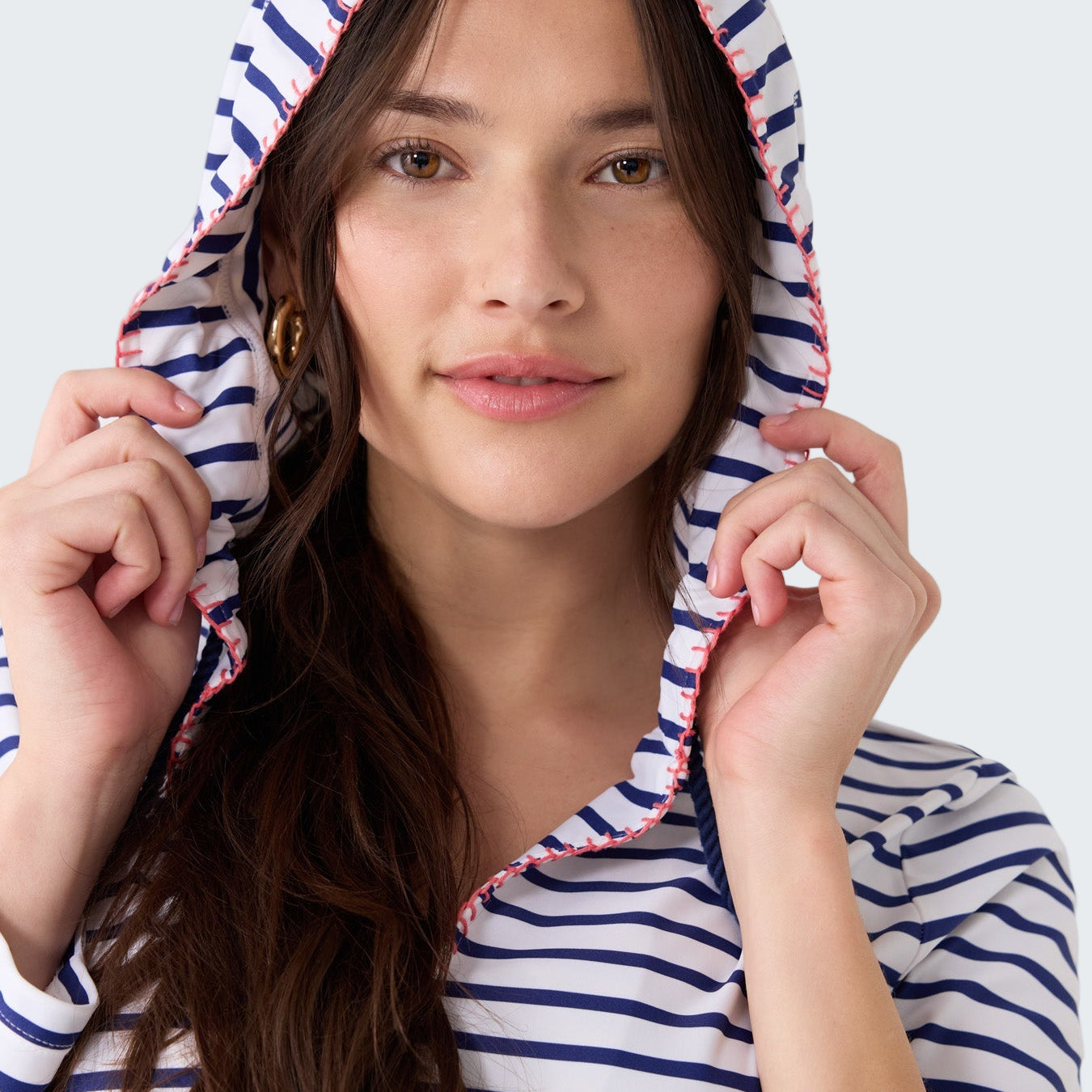 Woman wearing a blue and white striped hoodie with a hood on a light gray background