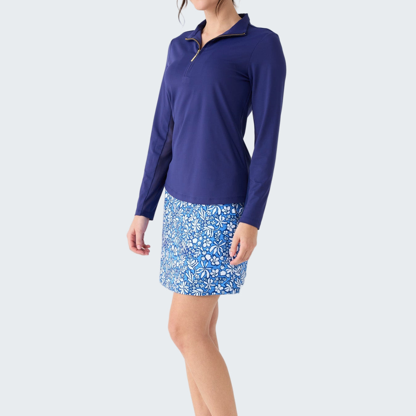 Woman wearing a blue long-sleeve top and floral skirt on a white background