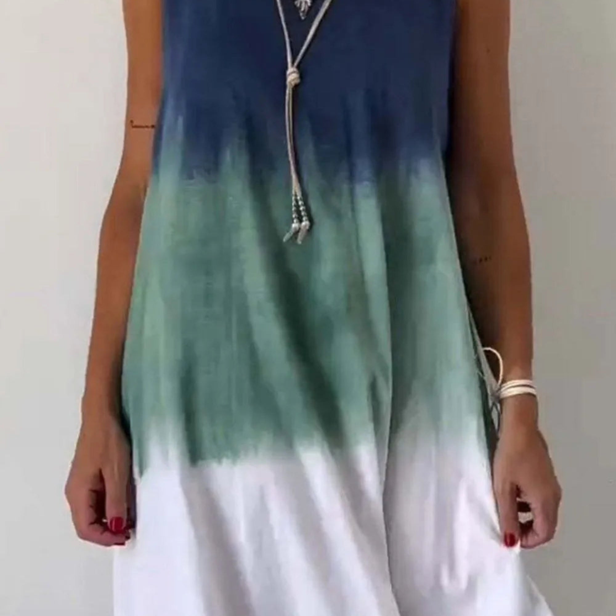 A sleeveless mini tank dress with tie-dye patterns in blue and green shades on a white background.
