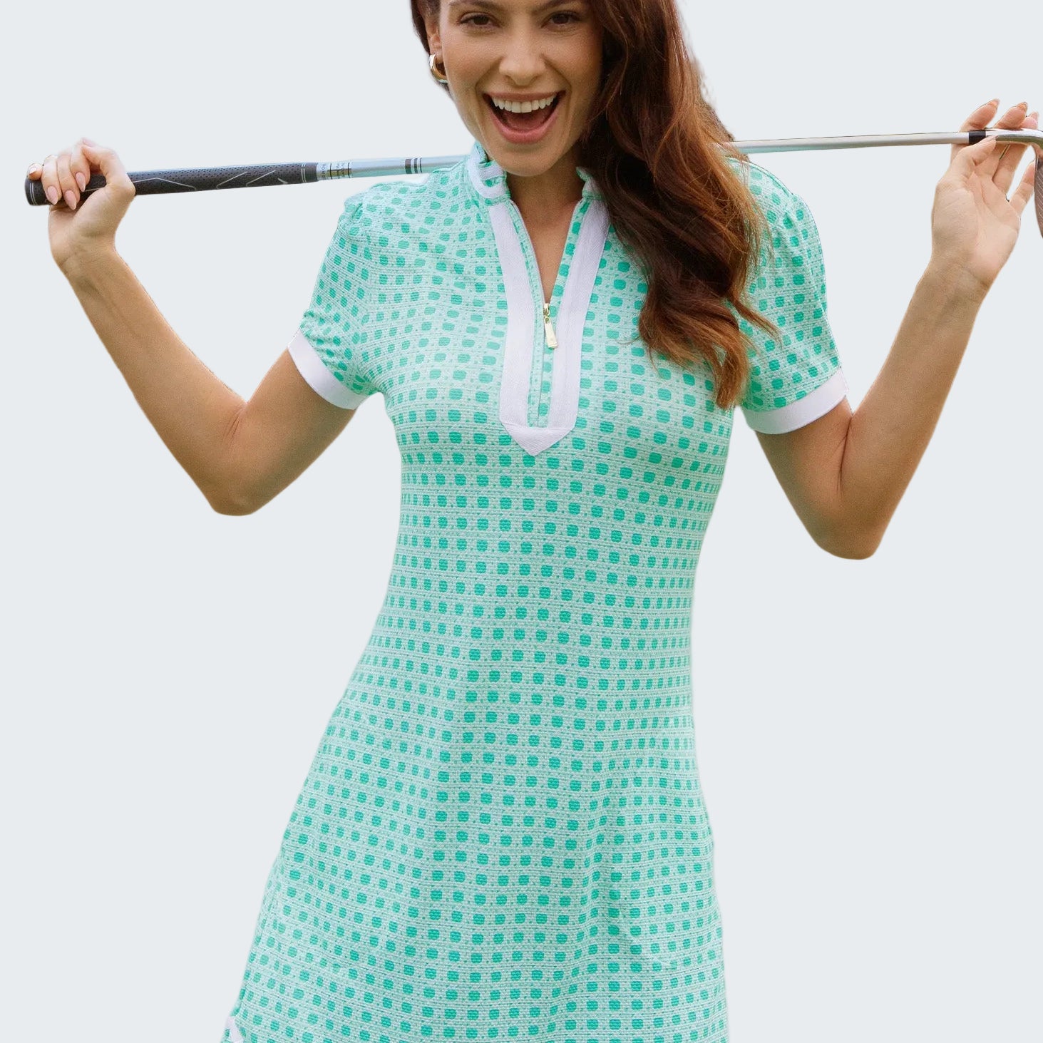 Woman in a green checkered dress holding a golf club on a golf course