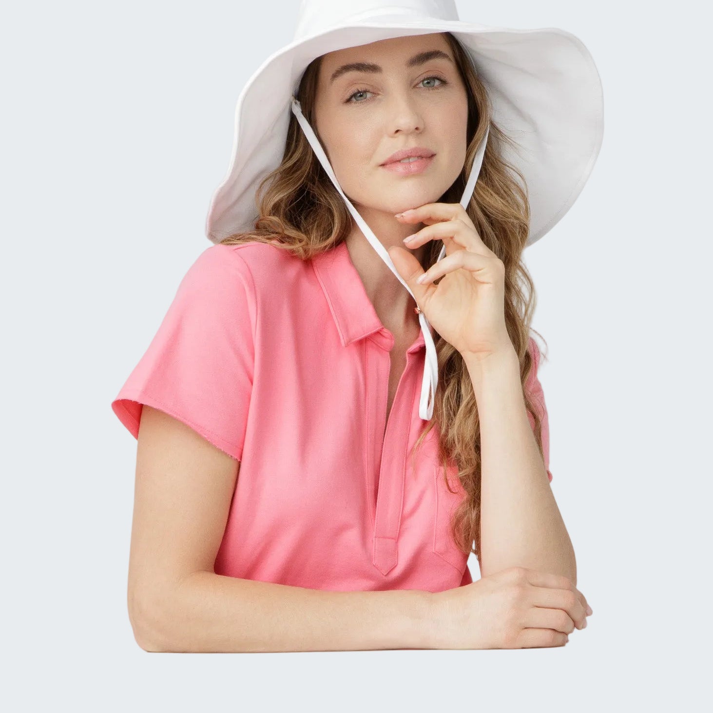 Woman wearing a white sun hat and pink shirt on a light gray background