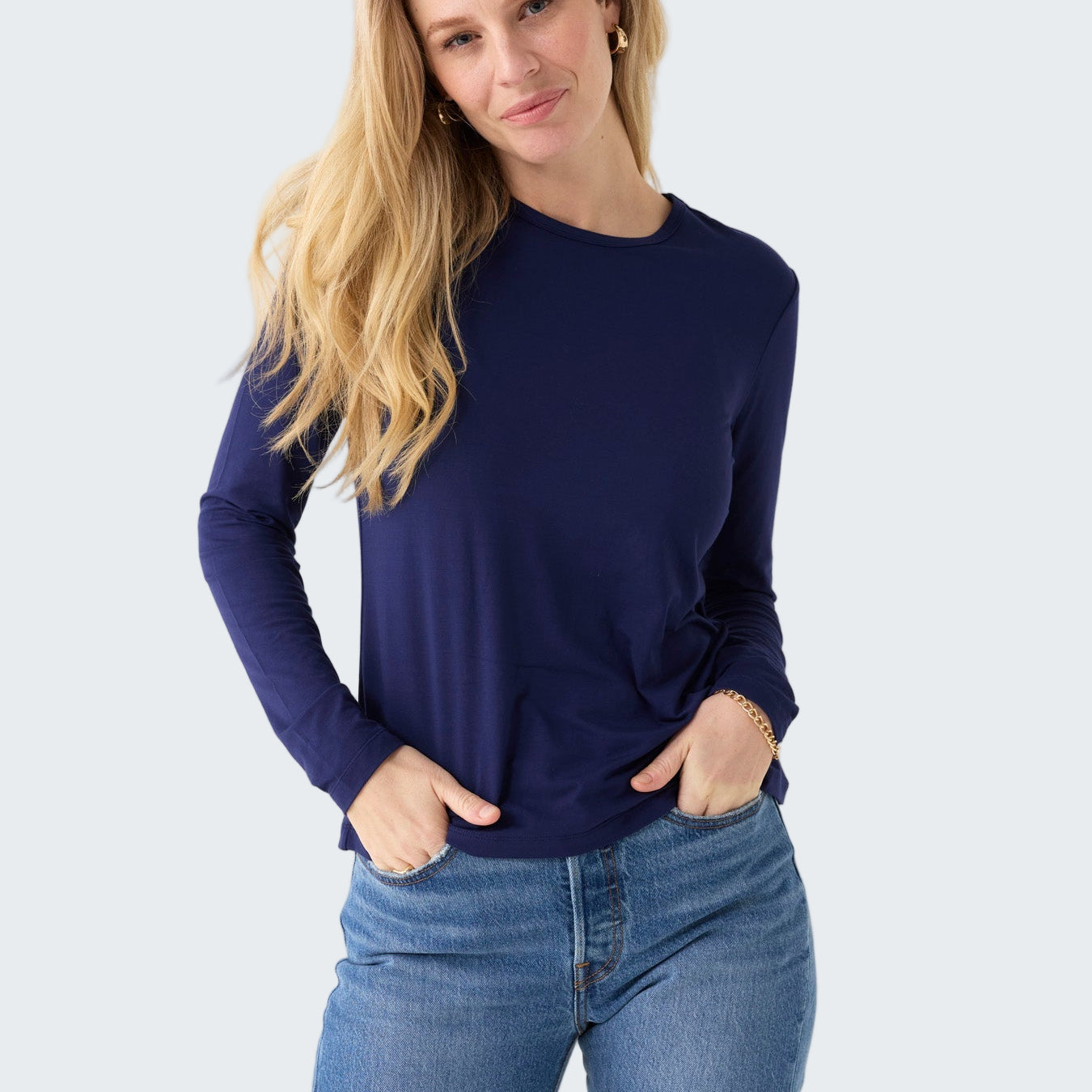 Woman wearing a navy long-sleeve top and blue jeans on a white background