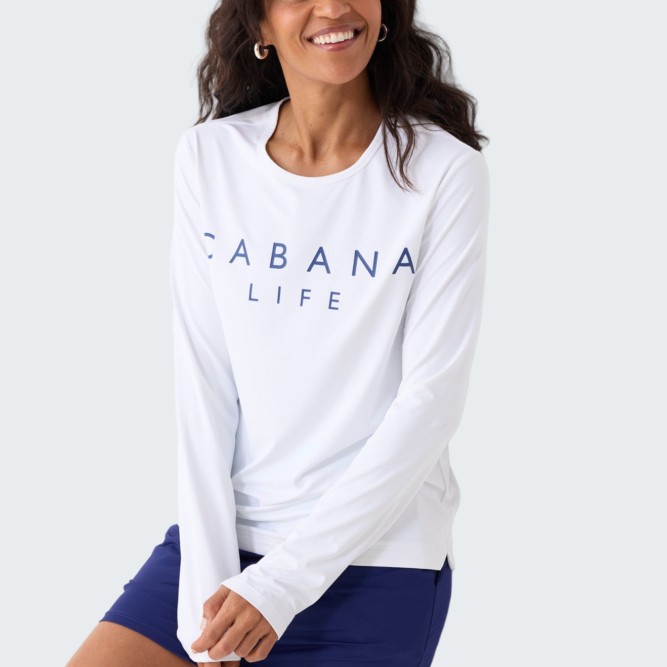 Woman wearing a white long-sleeve shirt with 'CABANA LIFE' text and blue shorts against a white background