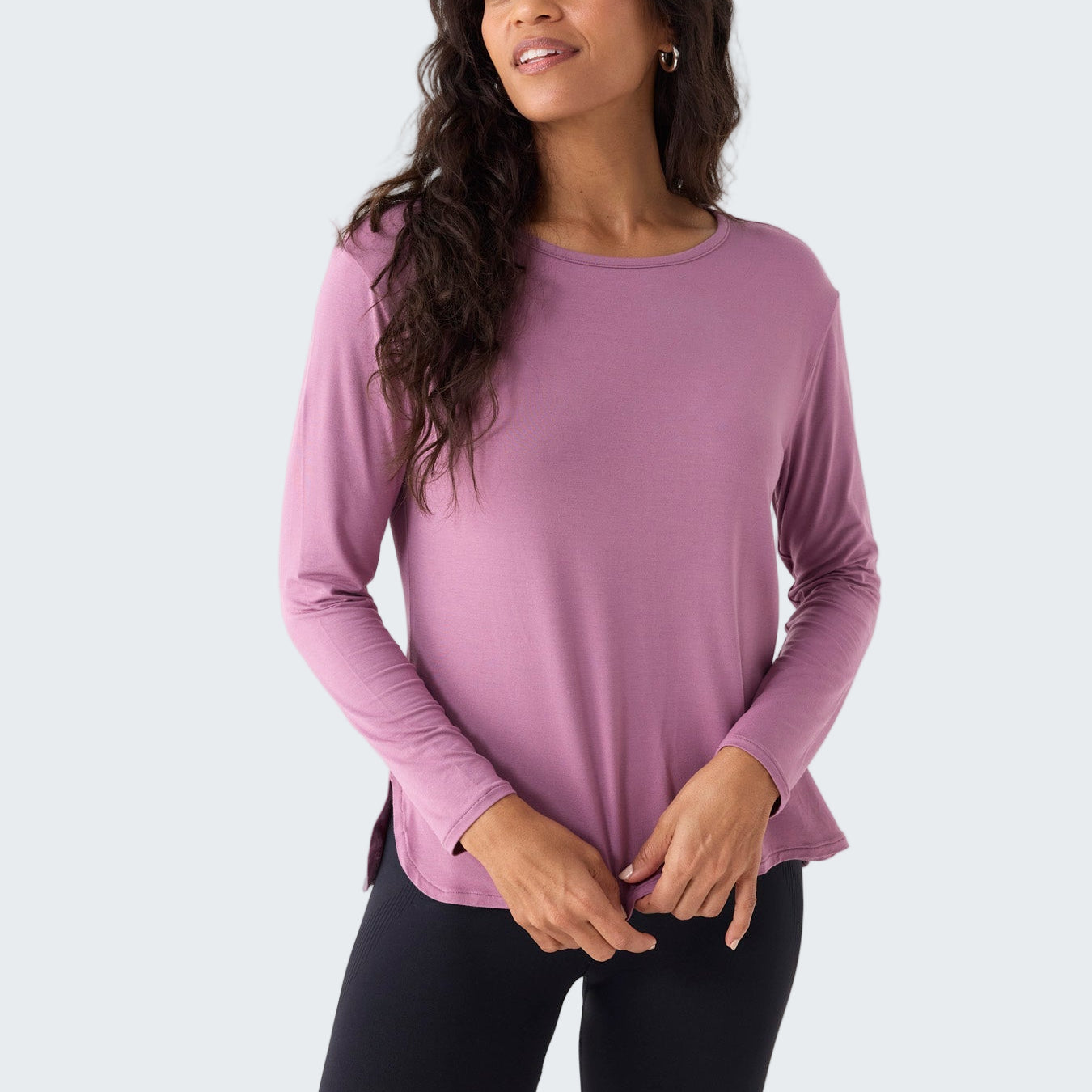 Woman wearing a pink long-sleeve top and black leggings on a white background