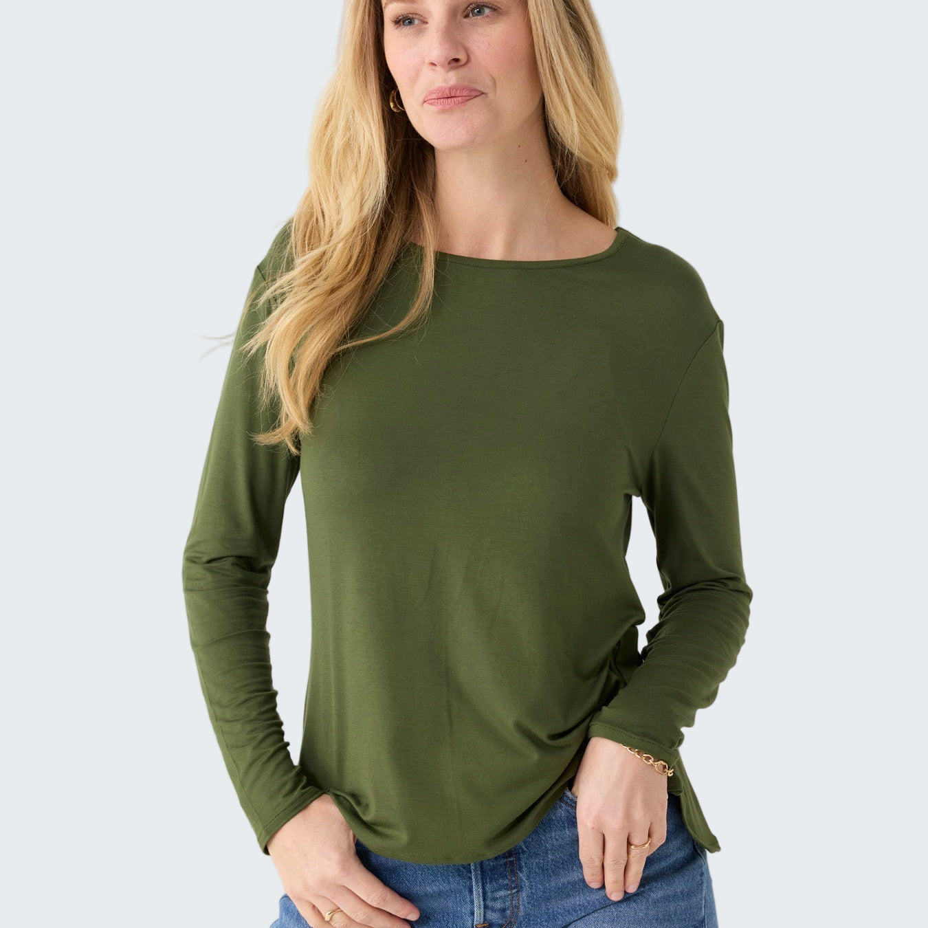 Woman wearing an olive green long-sleeve top and blue jeans on a white background