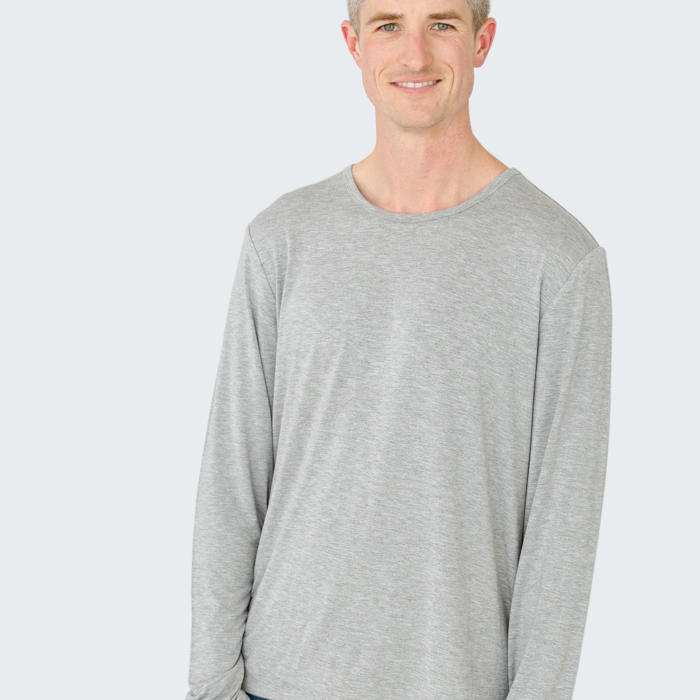 Man wearing a gray long-sleeve shirt and blue jeans on a white background