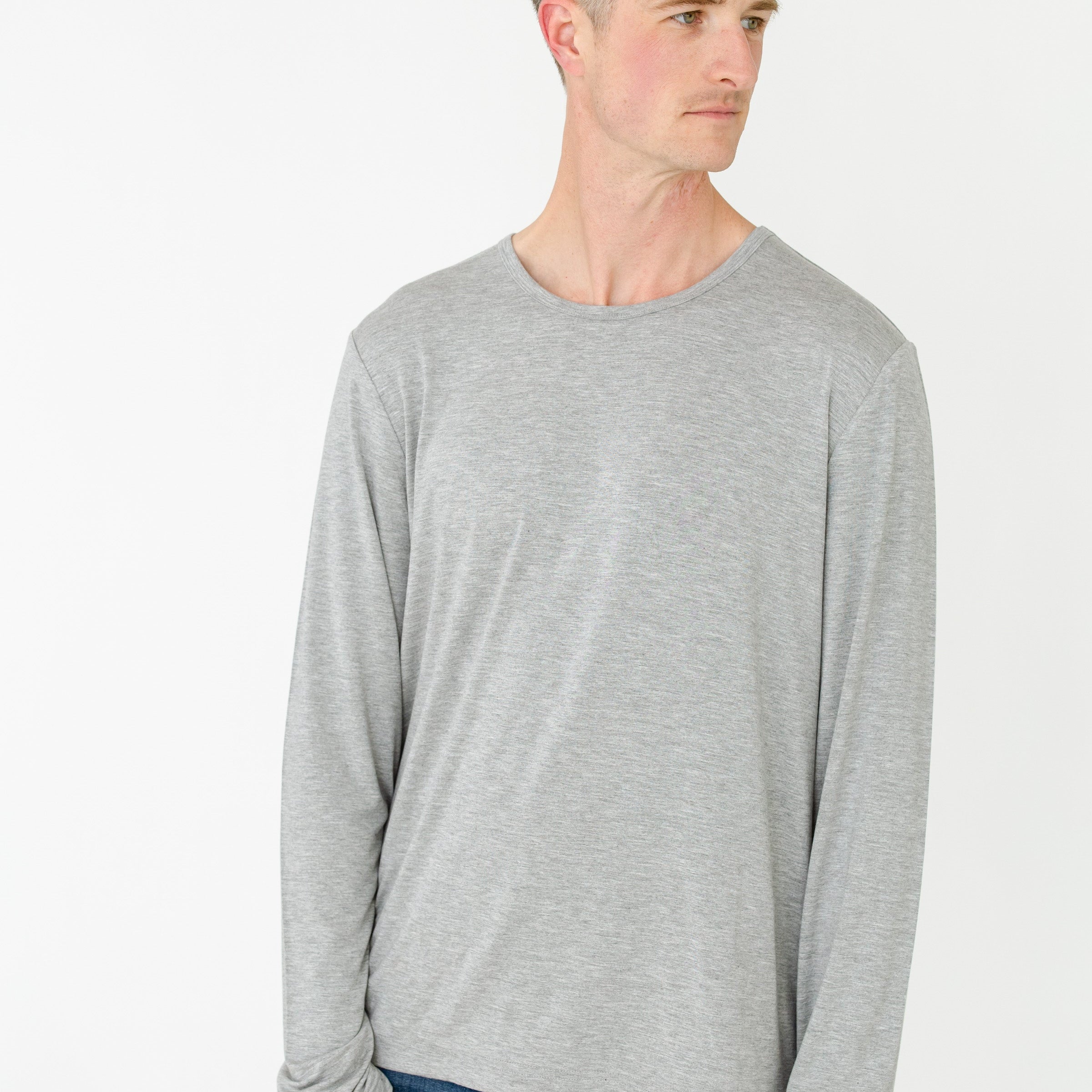 Man wearing a gray long-sleeve shirt and blue jeans on a white background