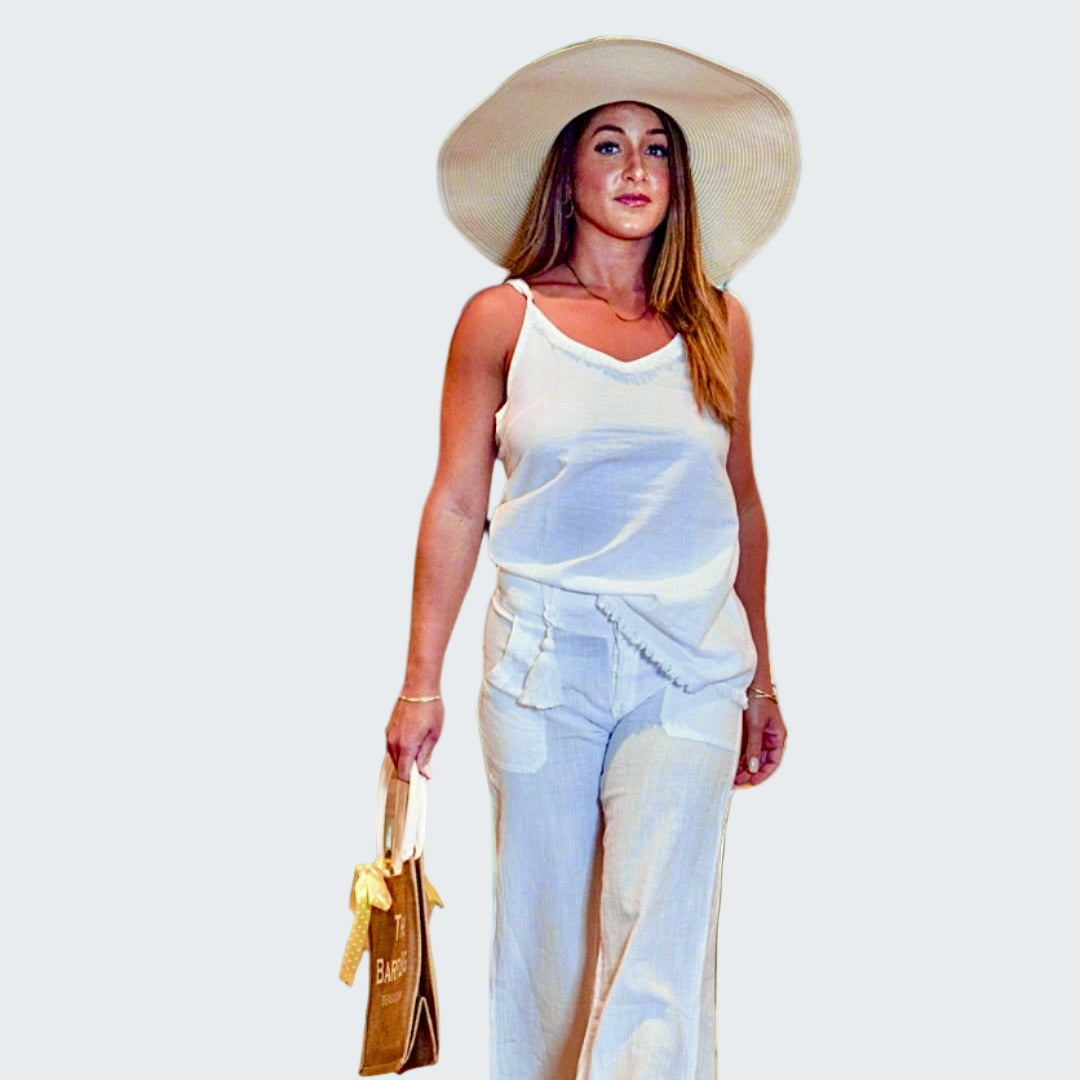 Woman in white outfit with sun hat walking on a beach with palm trees in the background