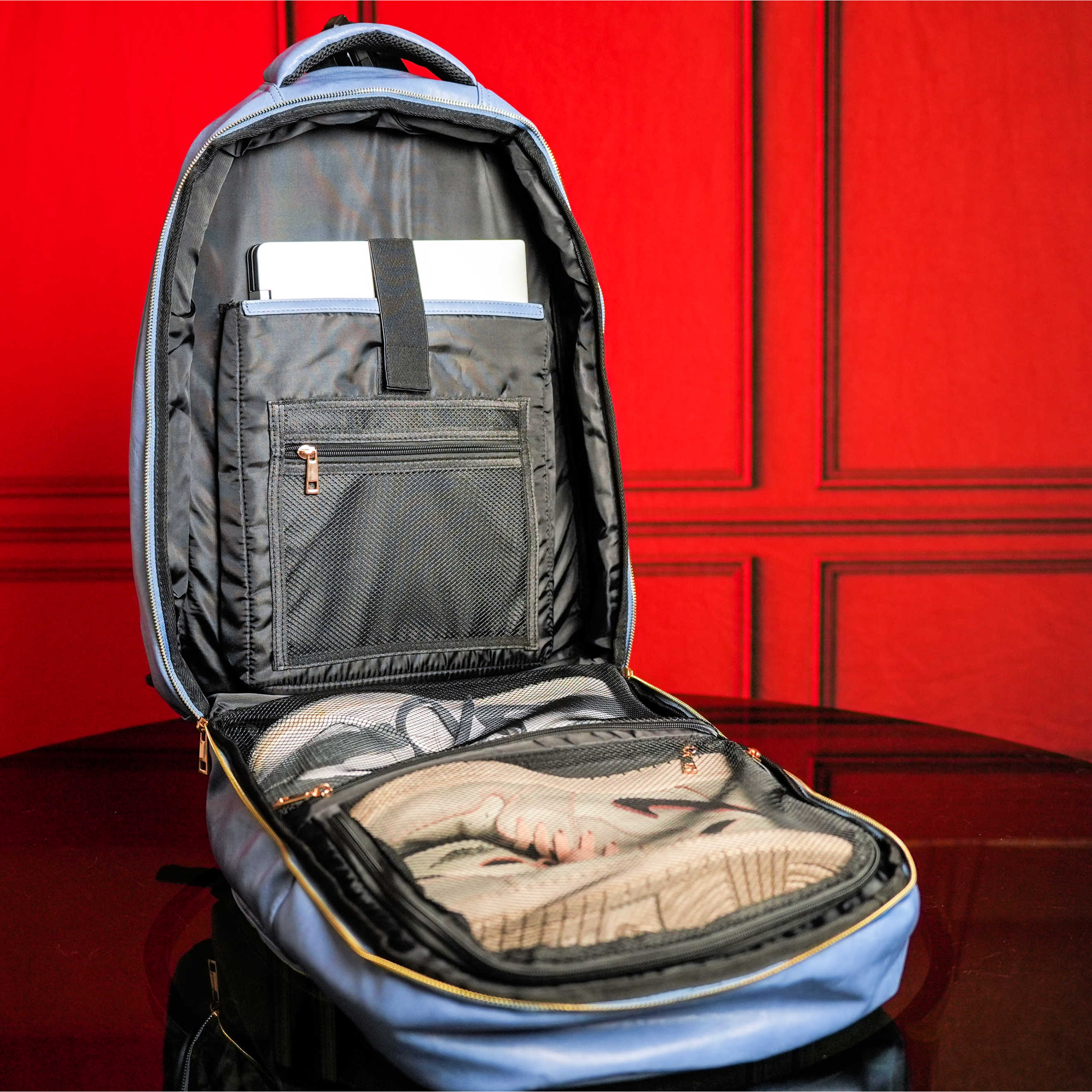 Blue backpack with open compartments against a red wall