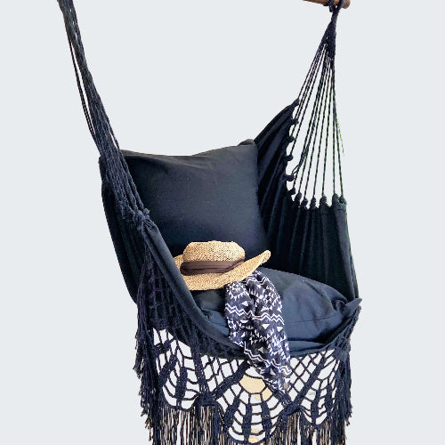 Black macrame hammock chair with pillows and a hat in a room setting.