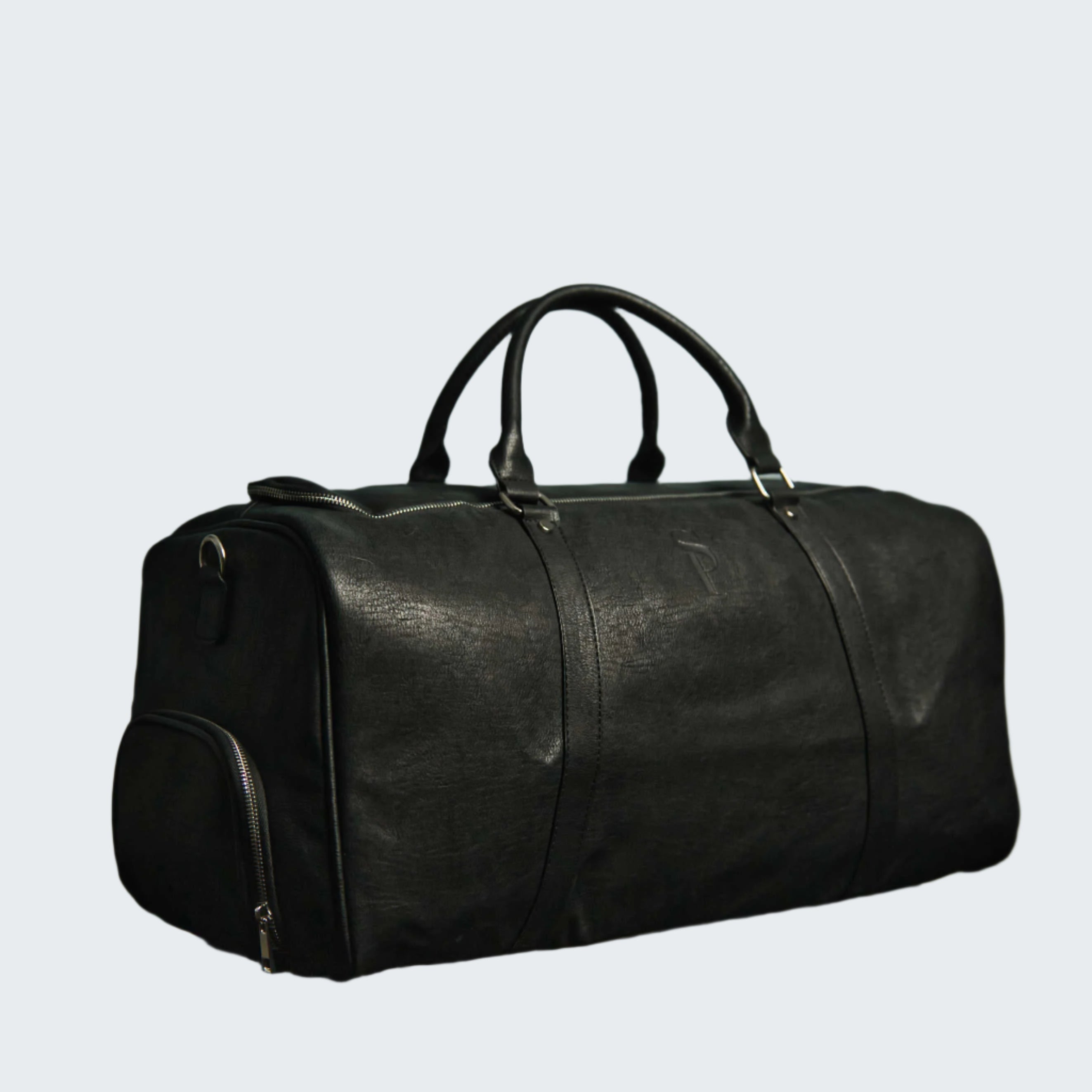 Black leather duffel bag on a reflective surface with a decorative wall in the background