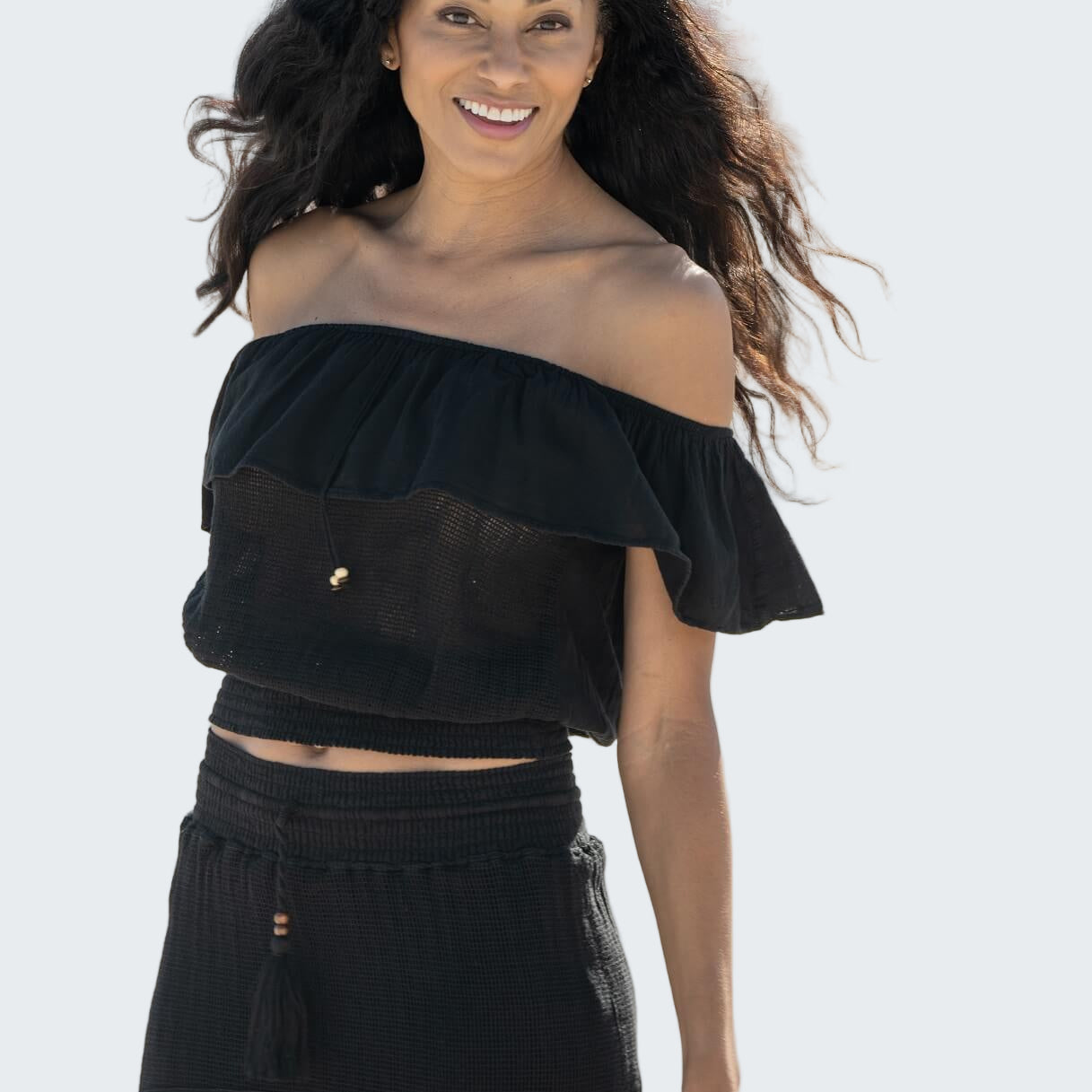 Woman wearing a black off-shoulder top and skirt on a blurred outdoor background
