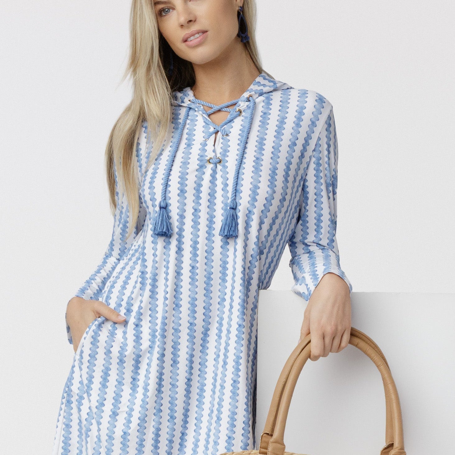Woman wearing a blue and white striped dress holding a straw bag against a white background