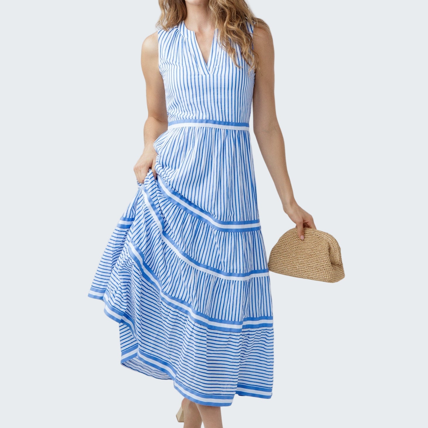 Woman wearing a blue and white striped dress holding a straw bag on a white background