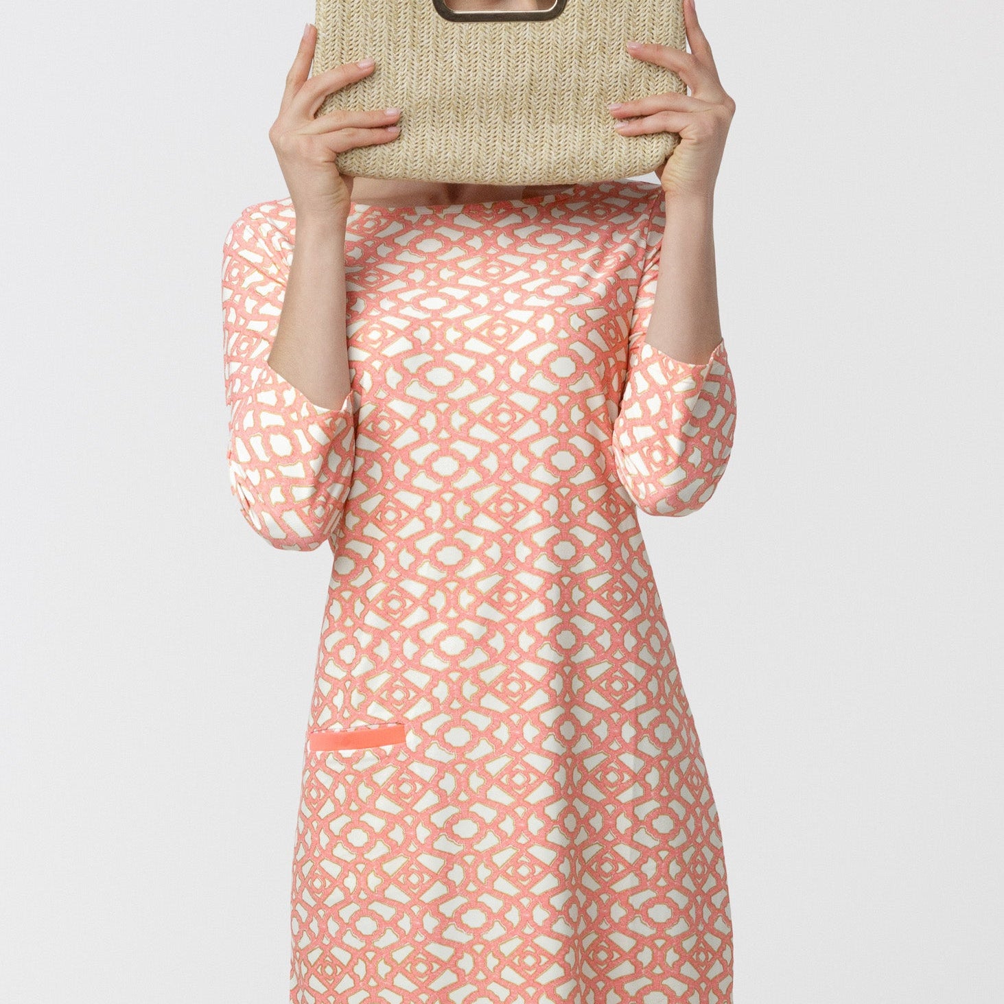 Woman wearing a patterned dress holding a woven bag against a white background