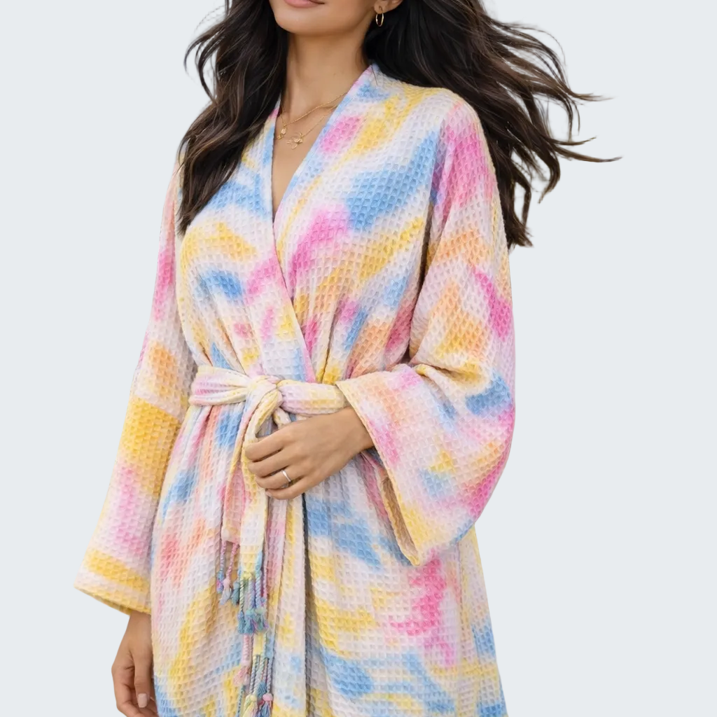 Woman wearing a colorful robe on a beach with ocean and house in the background