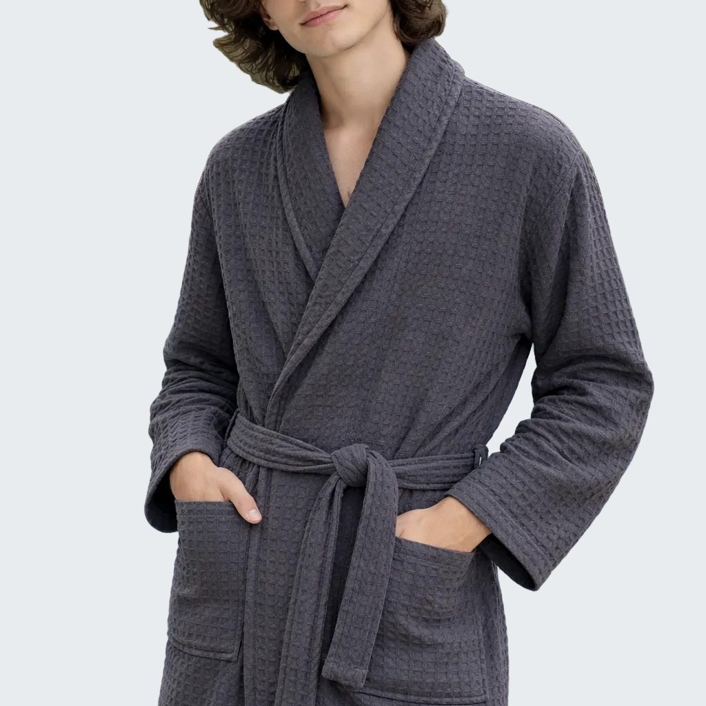 Man wearing a gray robe by a pool with palm trees in the background