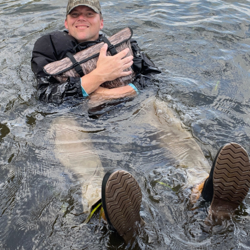 Person in waders holding a large fish in water
