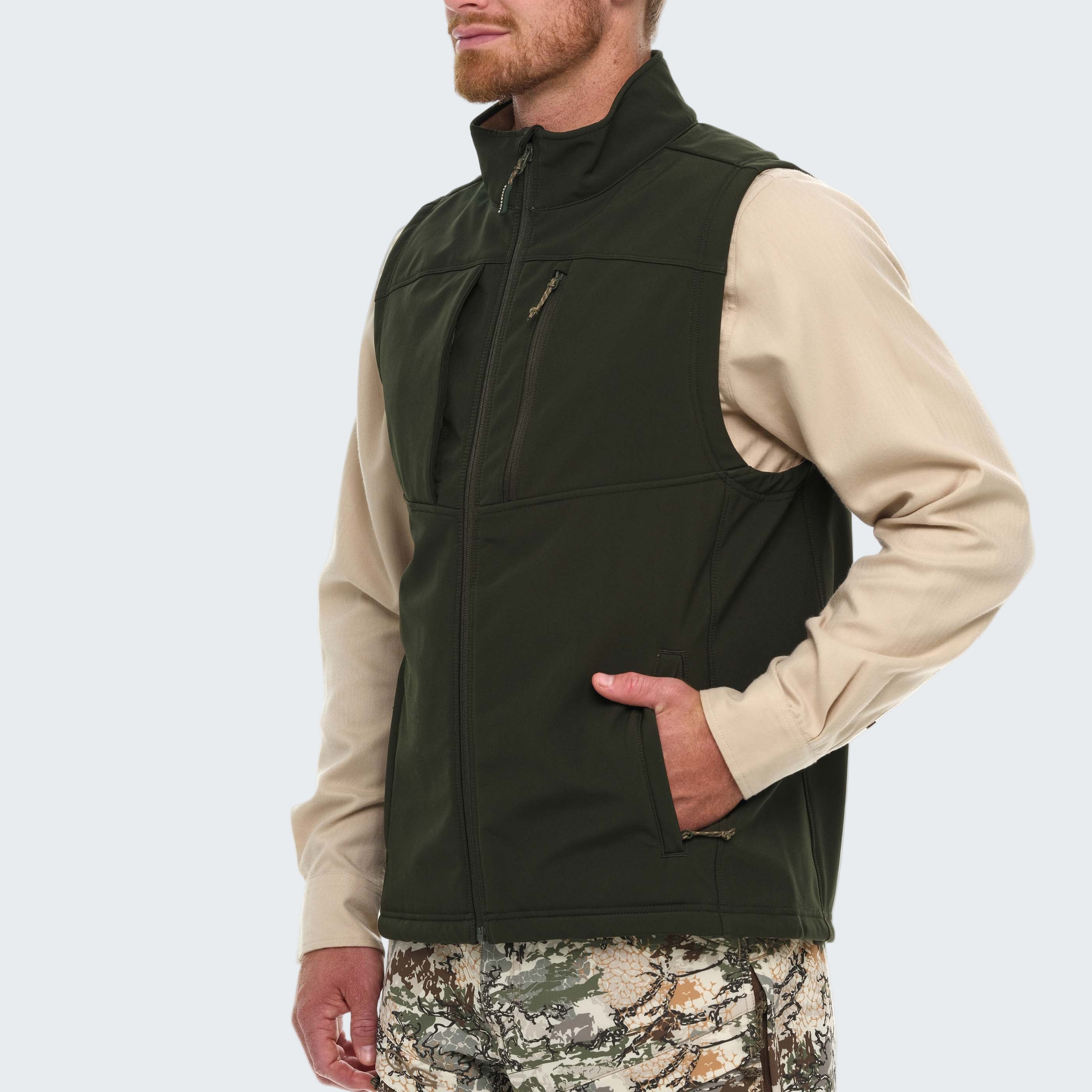 Man wearing a green vest over a beige shirt with camouflage pants on a white background