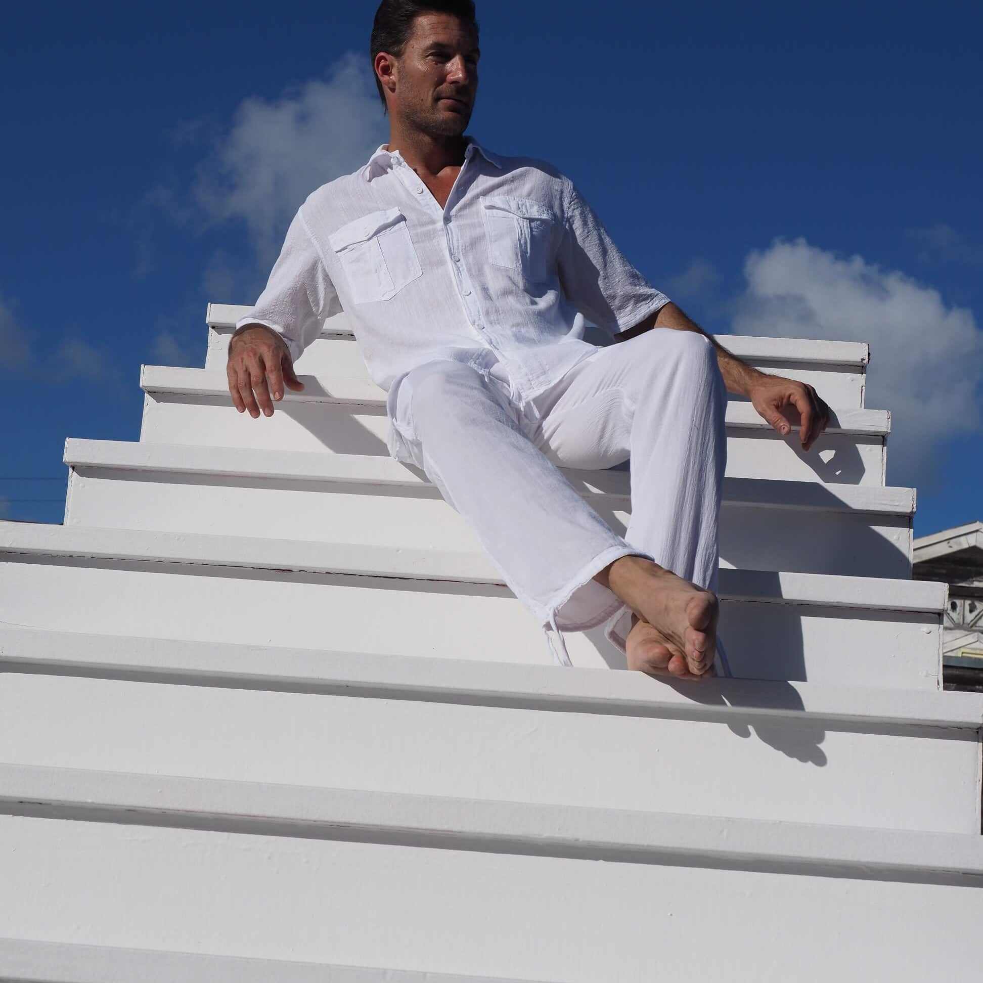 Man in white outfit sitting on a white staircase with a blue sky background