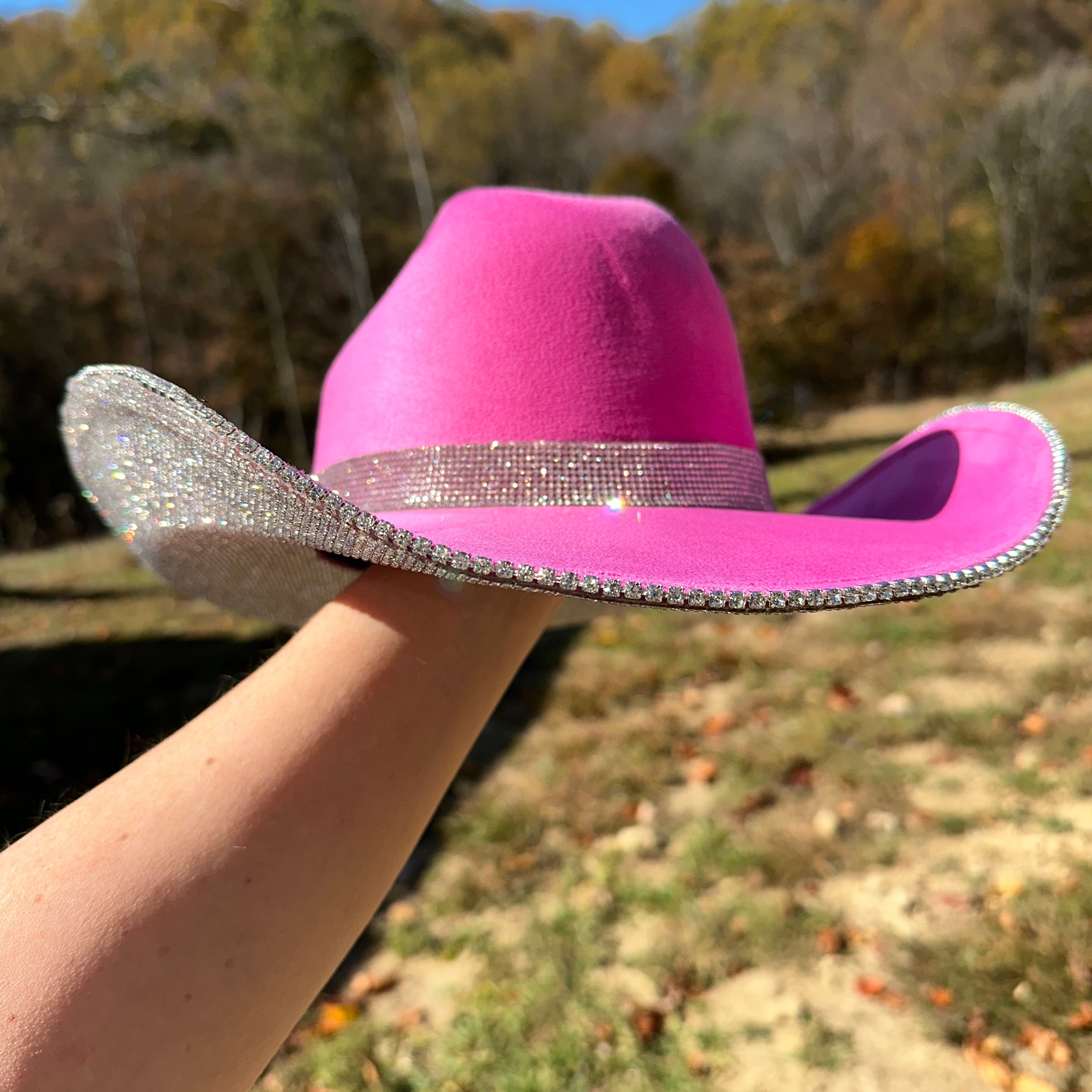 Pink cowboy hat with a glittery band held by a person outdoors.