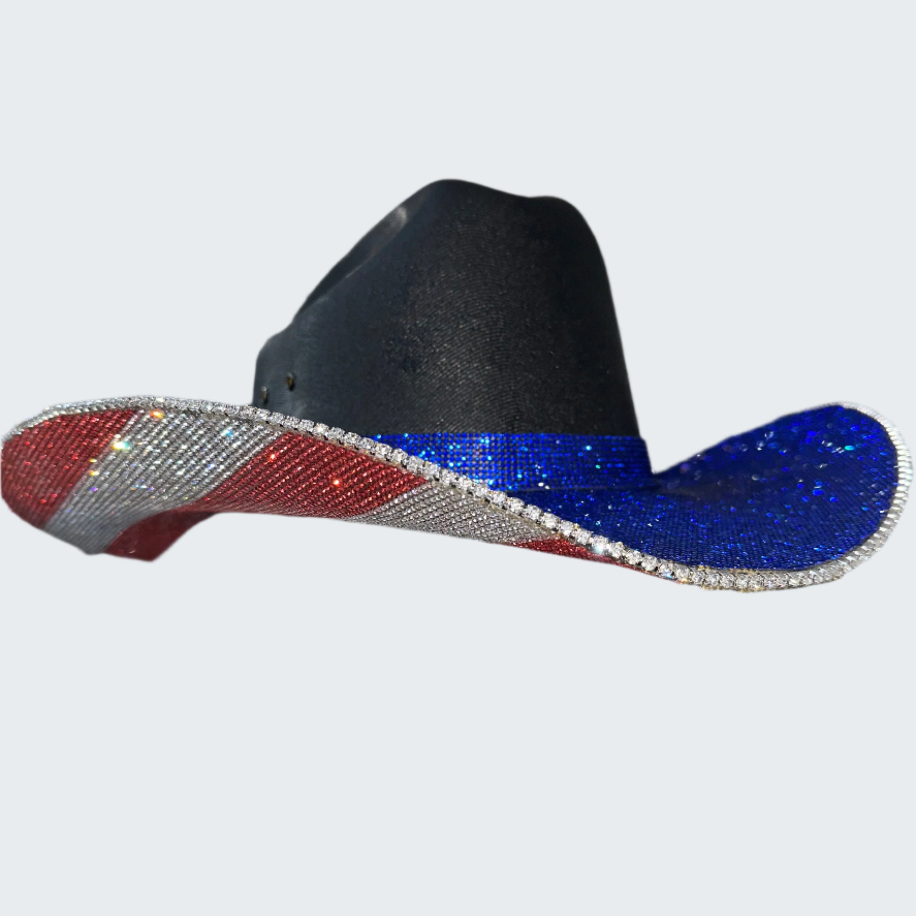 Black cowboy hat with red and blue glittery brim held by a gloved hand against a silver sequin background.
