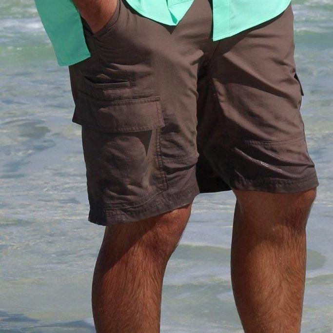 Person wearing a light green shirt and brown shorts standing in shallow water.